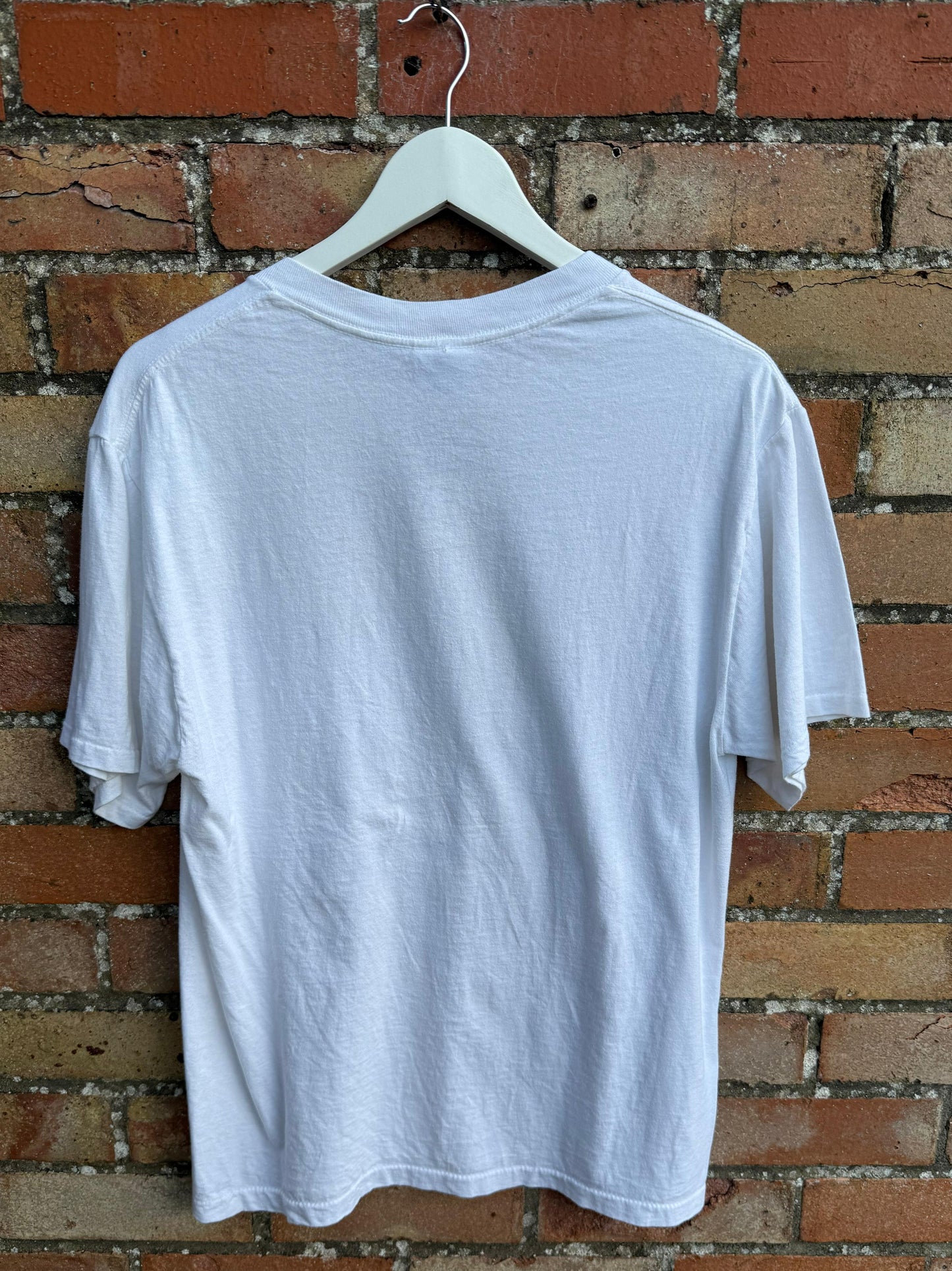 White t-shirt on a hanger against a brick wall