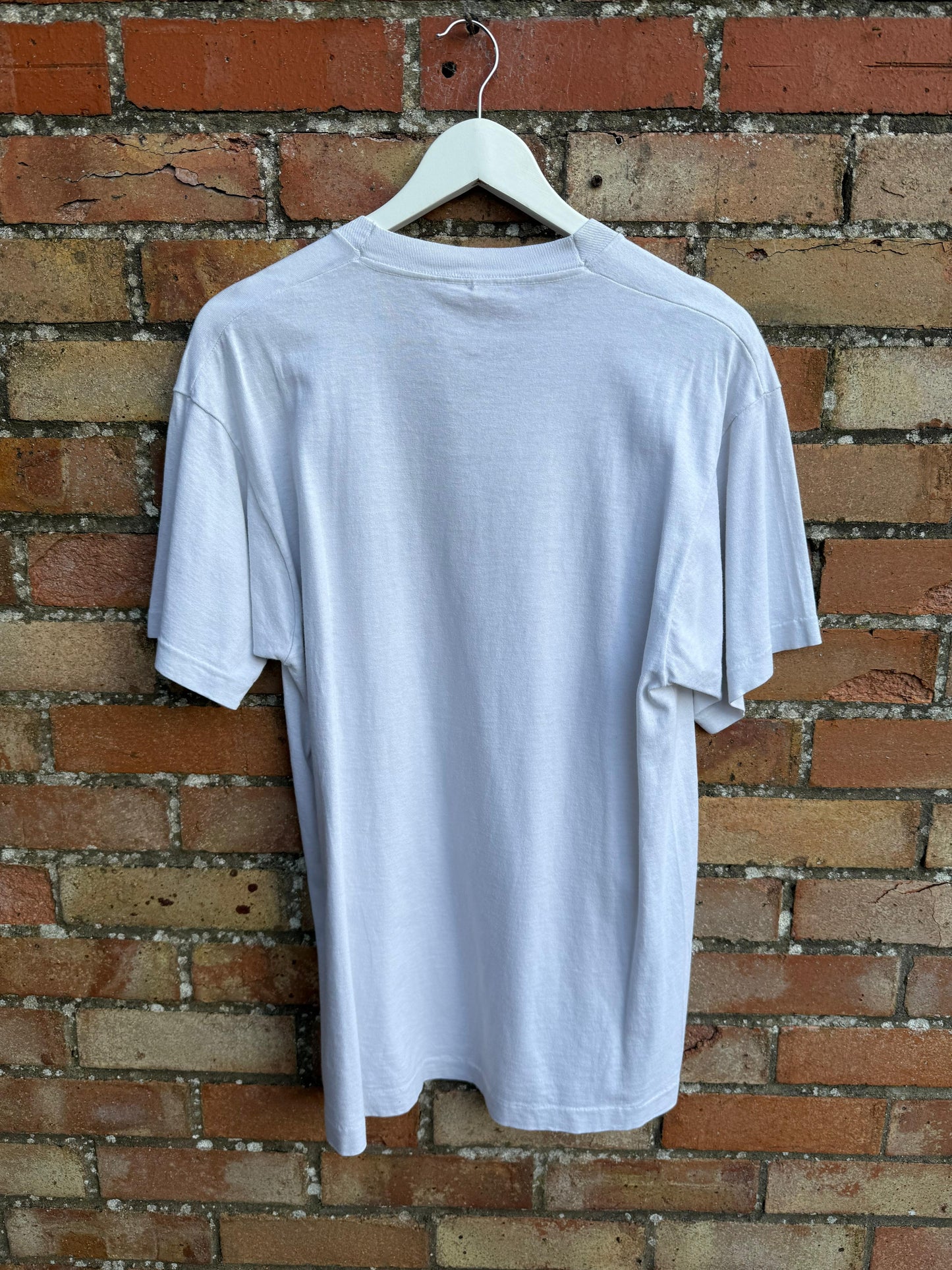 Back view of white t-shirt on a hanger against a brick wall