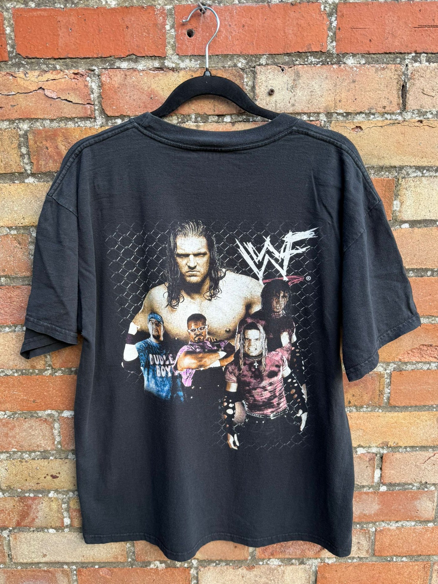 Black t-shirt with WWF graphic on a hanger against a brick wall.