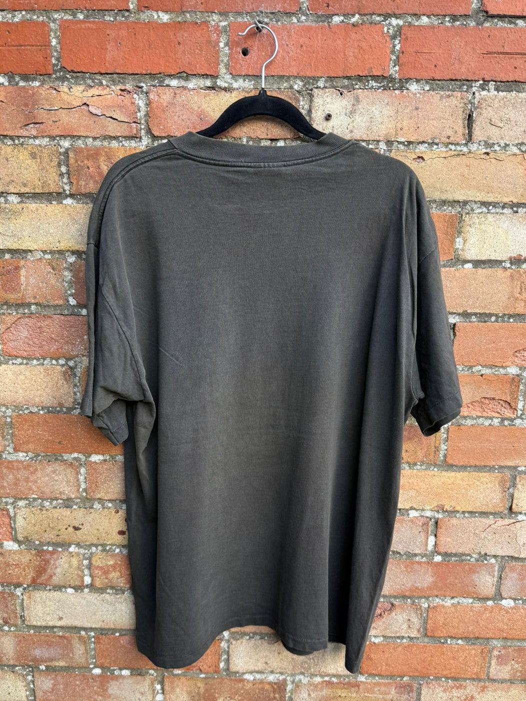 Black t-shirt on a hanger against a brick wall