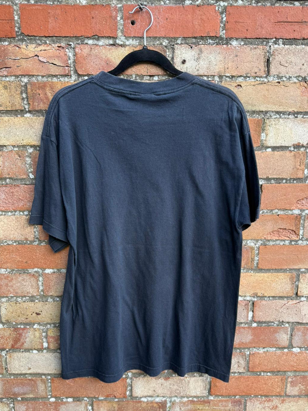 back of a black t-shirt hanging against a brick wall