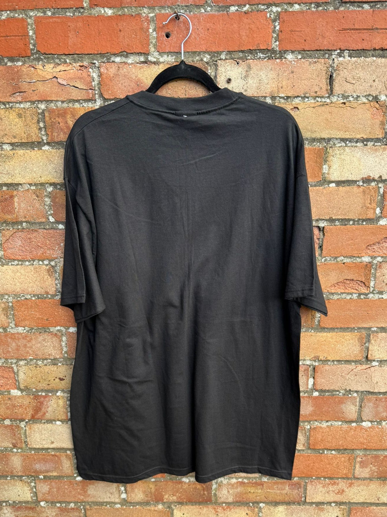 Black t-shirt on a hanger against a brick wall