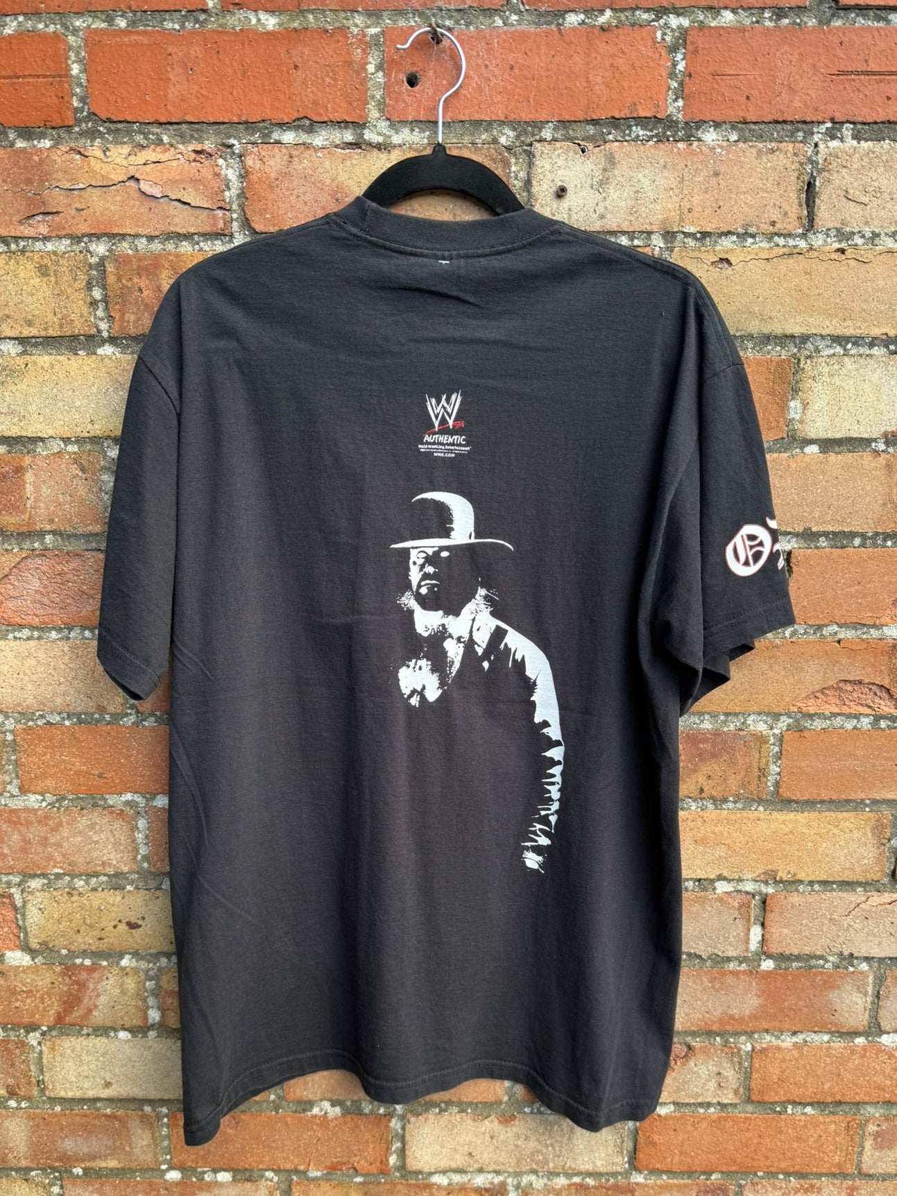 Black t-shirt with a graphic design on a hanger against a brick wall