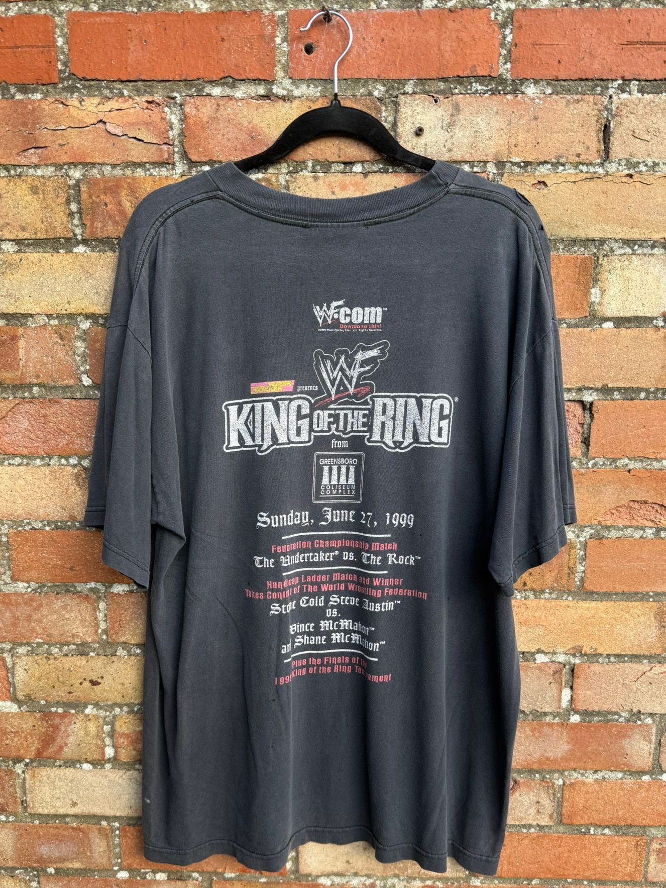 Back view of faded black t-shirt with WWF branding and King of the Ring text on a brick wall background