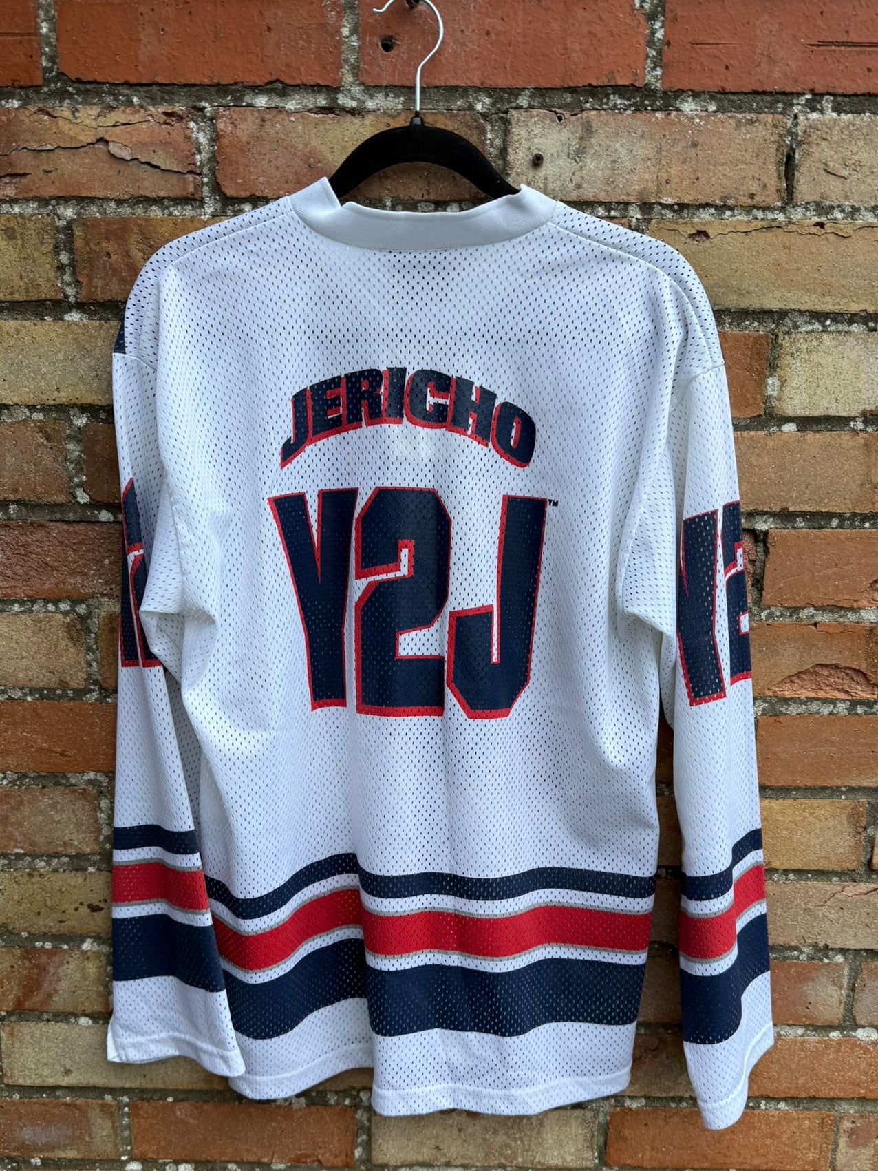 White sports jersey with 'Jericho' and 'Y2J' text, hanging on a brick wall.
