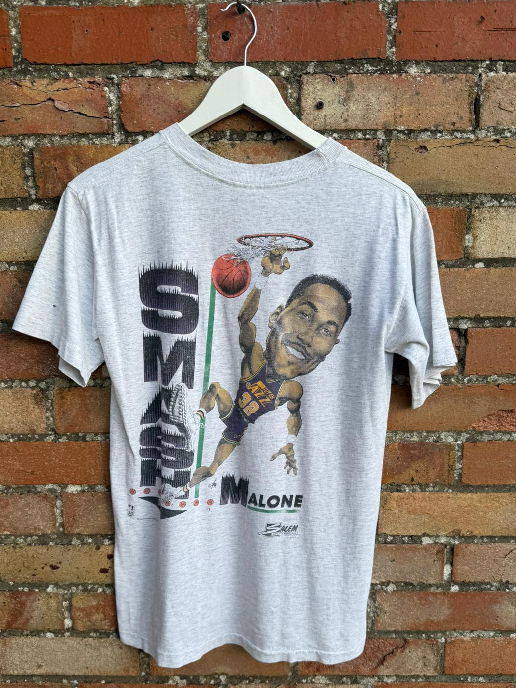 Back print t-shirt with a graphic design of basketball player Malone hanging on a brick wall.