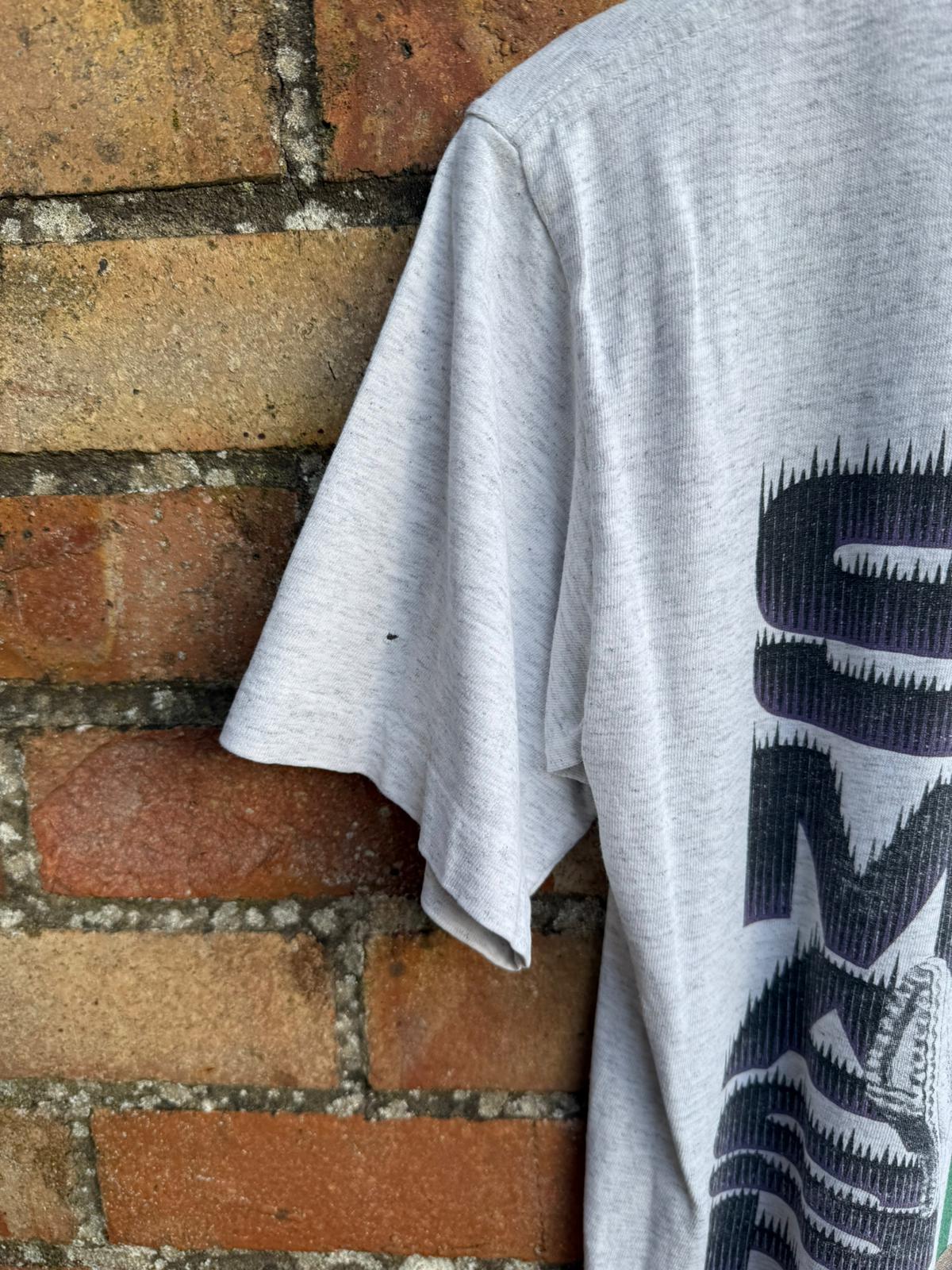 Close-up of gray t-shirt sleeve showing small pinhole,  up against a brick wall