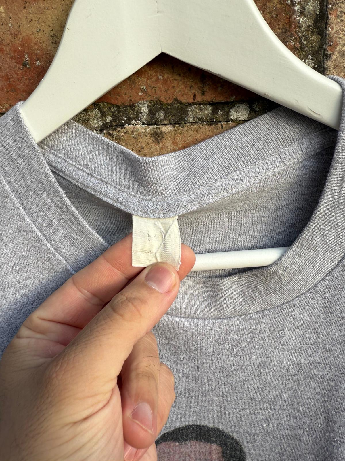 Gray shirt with a hand holding a white label against a textured background