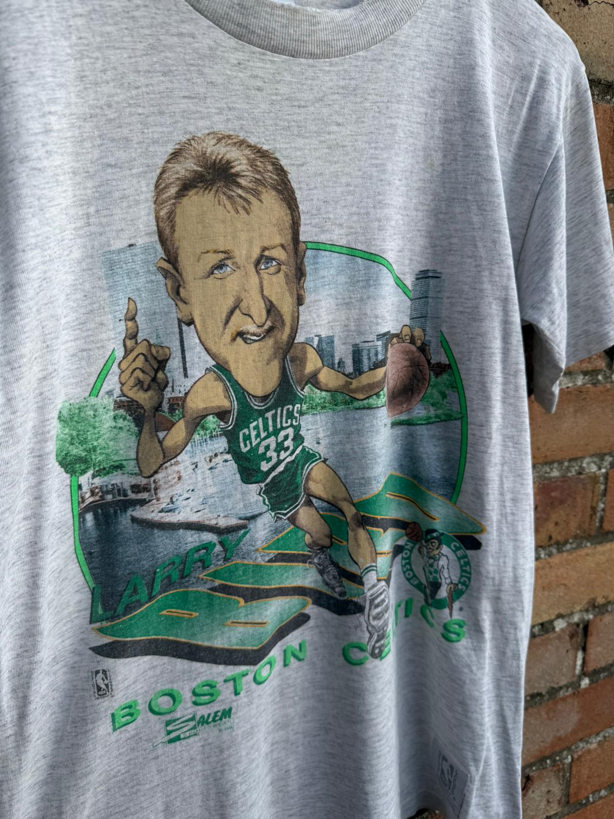 Gray t-shirt with Boston Celtics caricature of Larry Bird in a Celtics jersey on a brick wall background