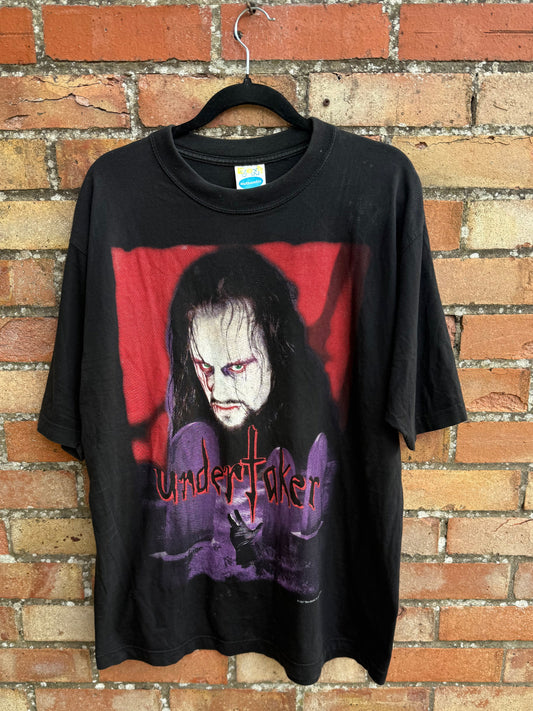 Black t-shirt with The Undertaker graphic design hanging on a brick surface