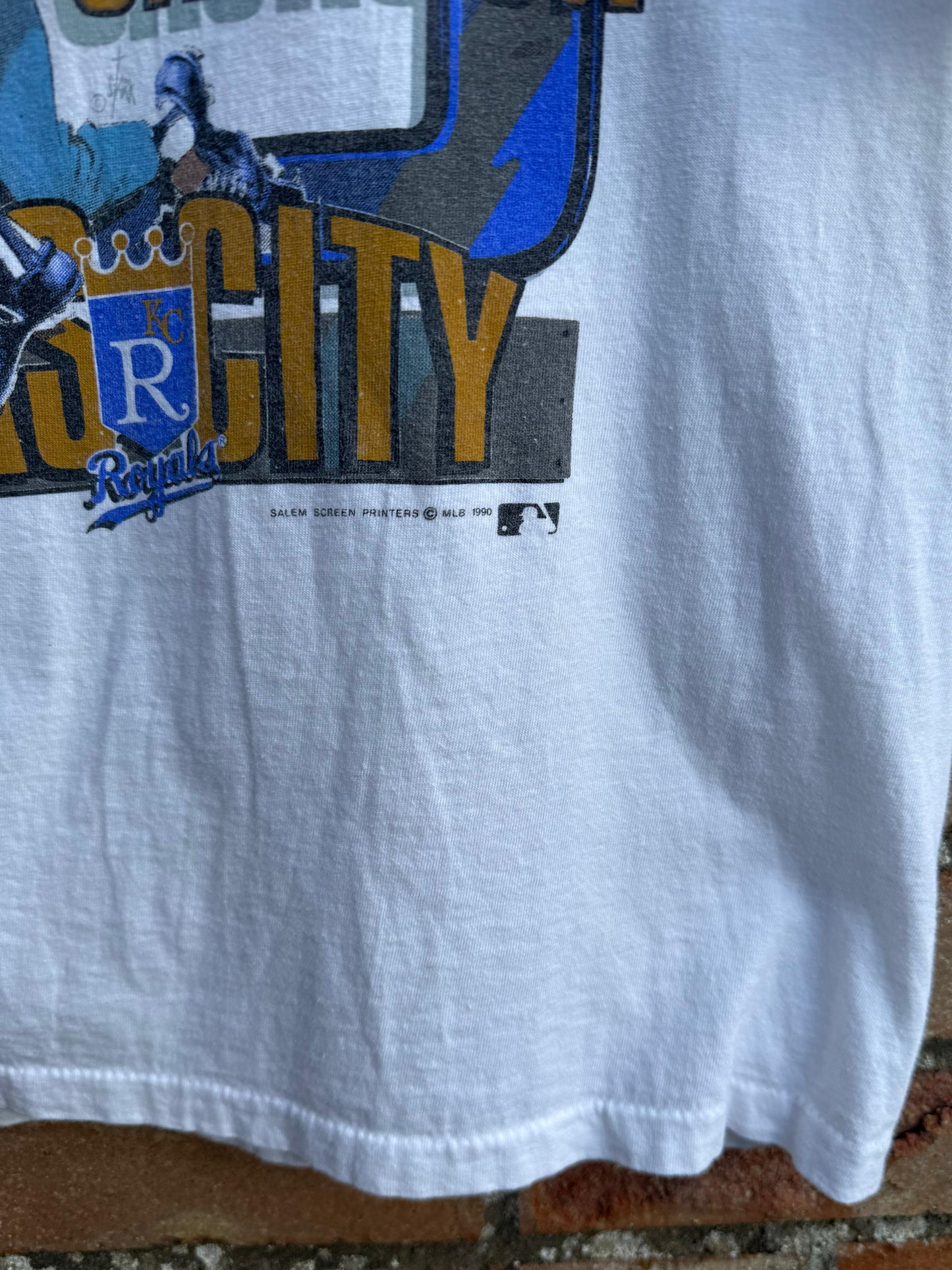 White t-shirt with 'Royals' text and copyright Salem 1990, hanging on a brick surface