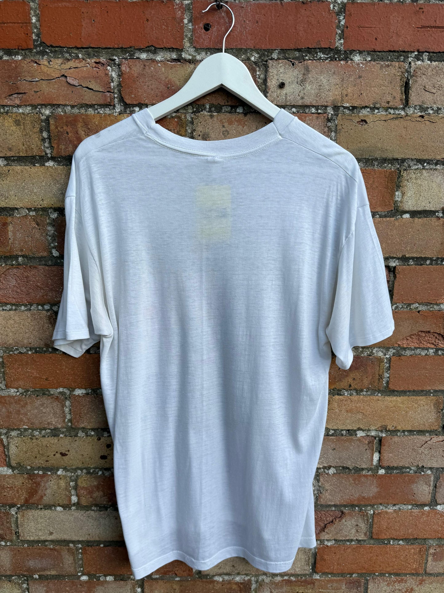 White t-shirt on a hanger against a brick wall
