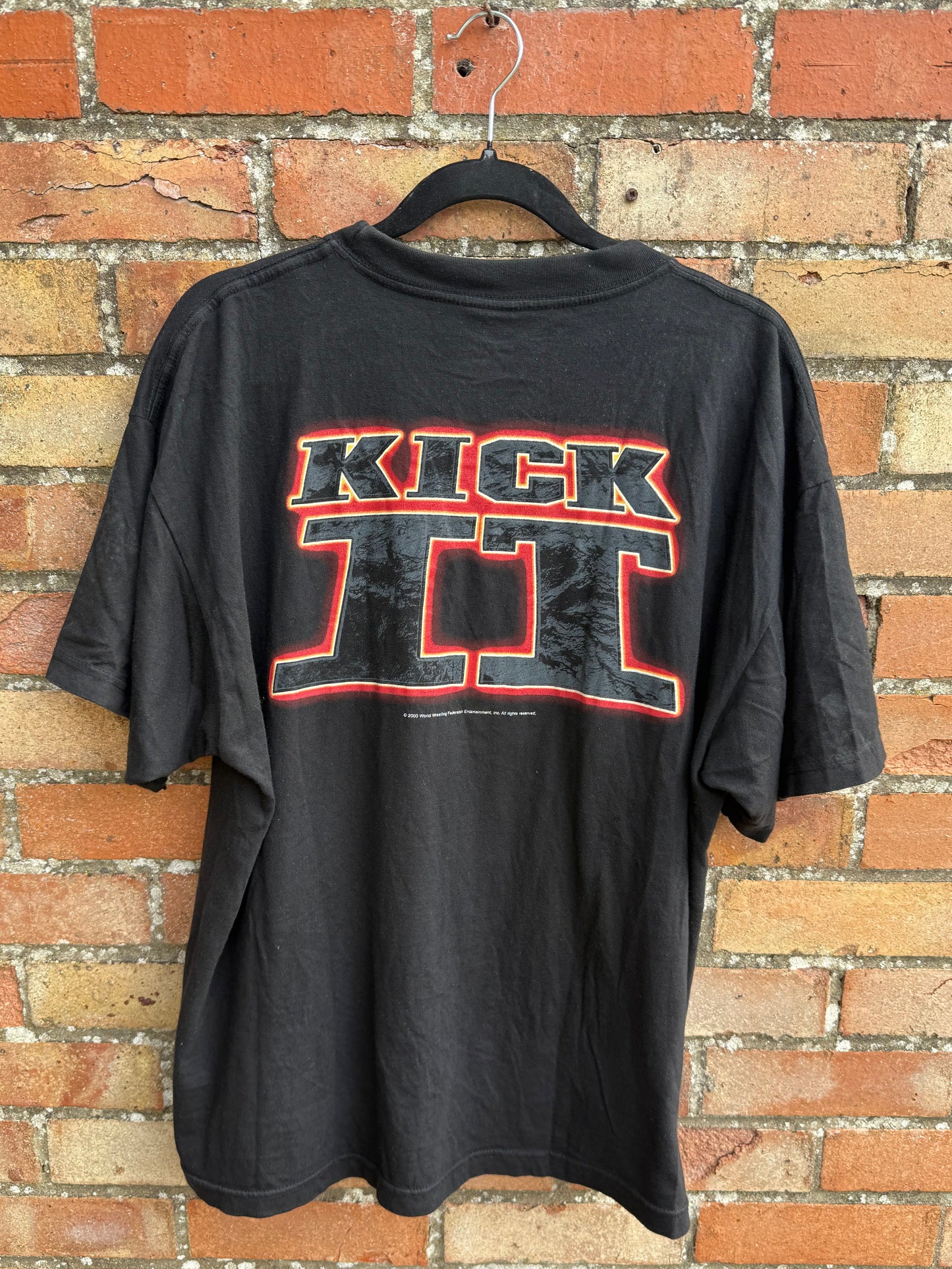 Black t-shirt with red and white text Kick It on a brick surface