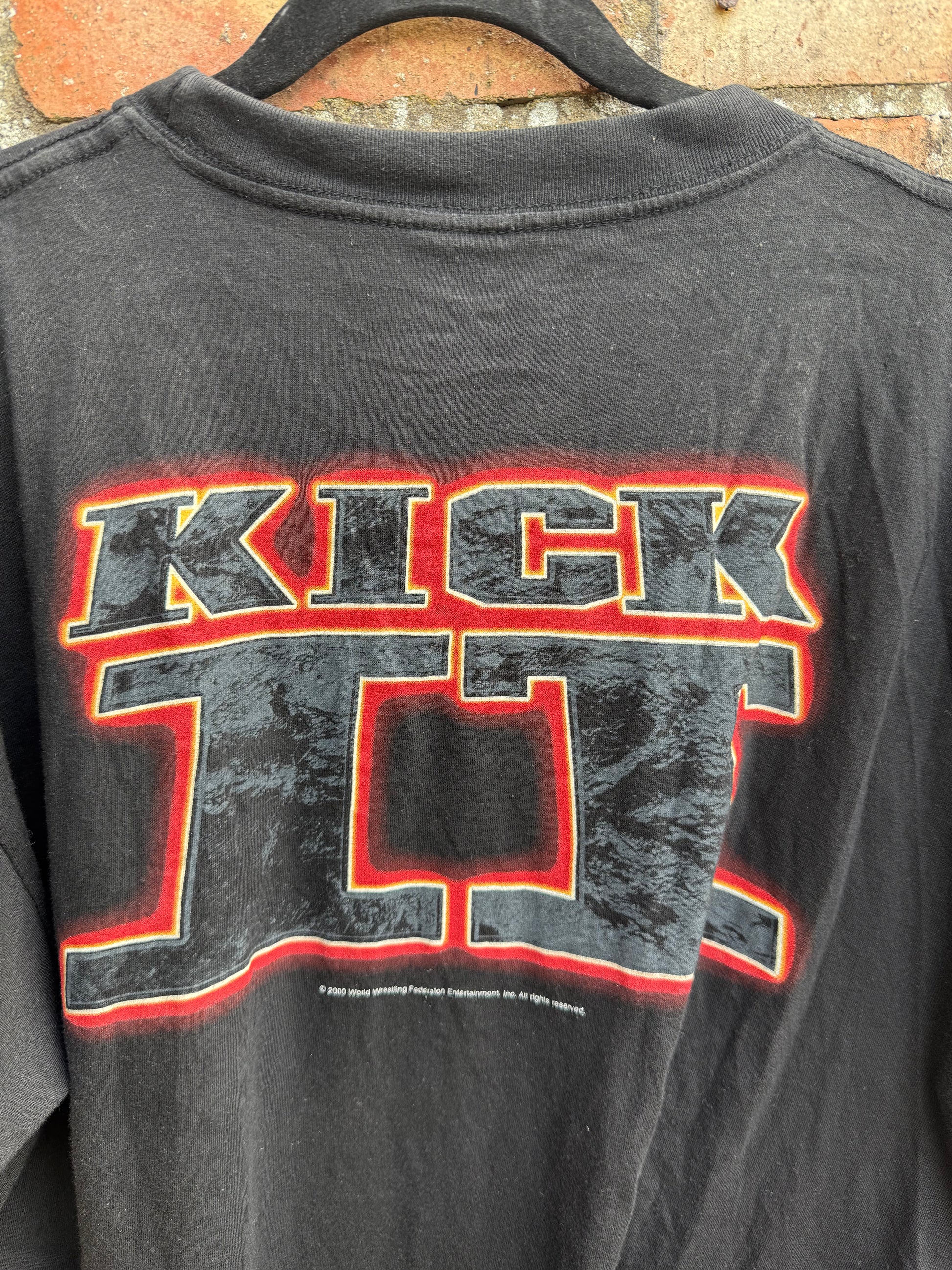 Close-up of Kick It graphic on the reverse of a black t-shirt on a hanger