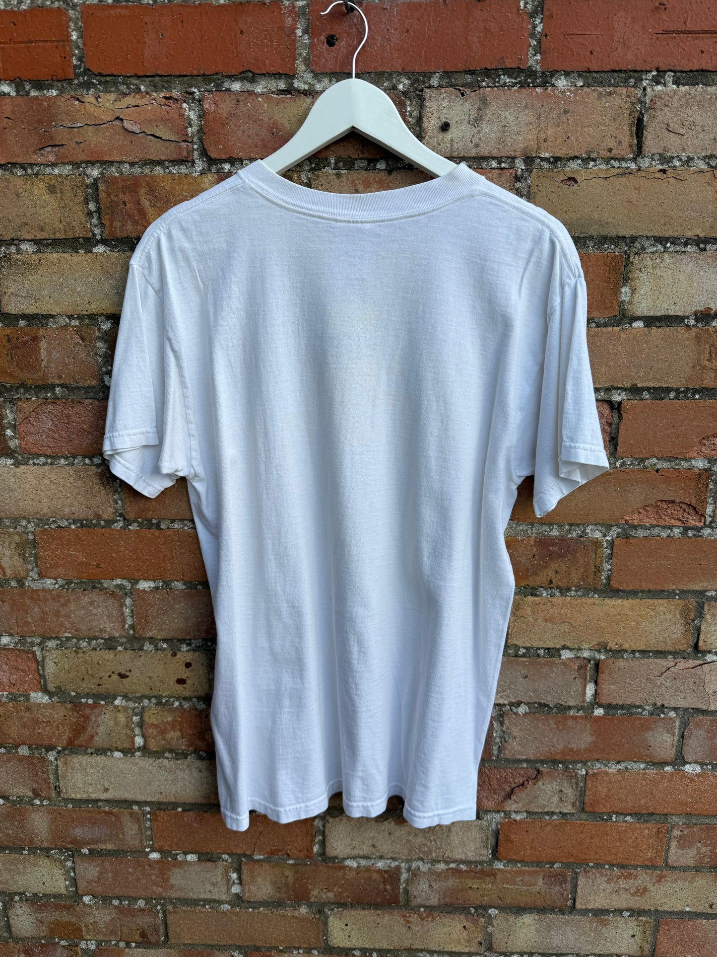 The back of a white t-shirt on a hanger against a brick wall