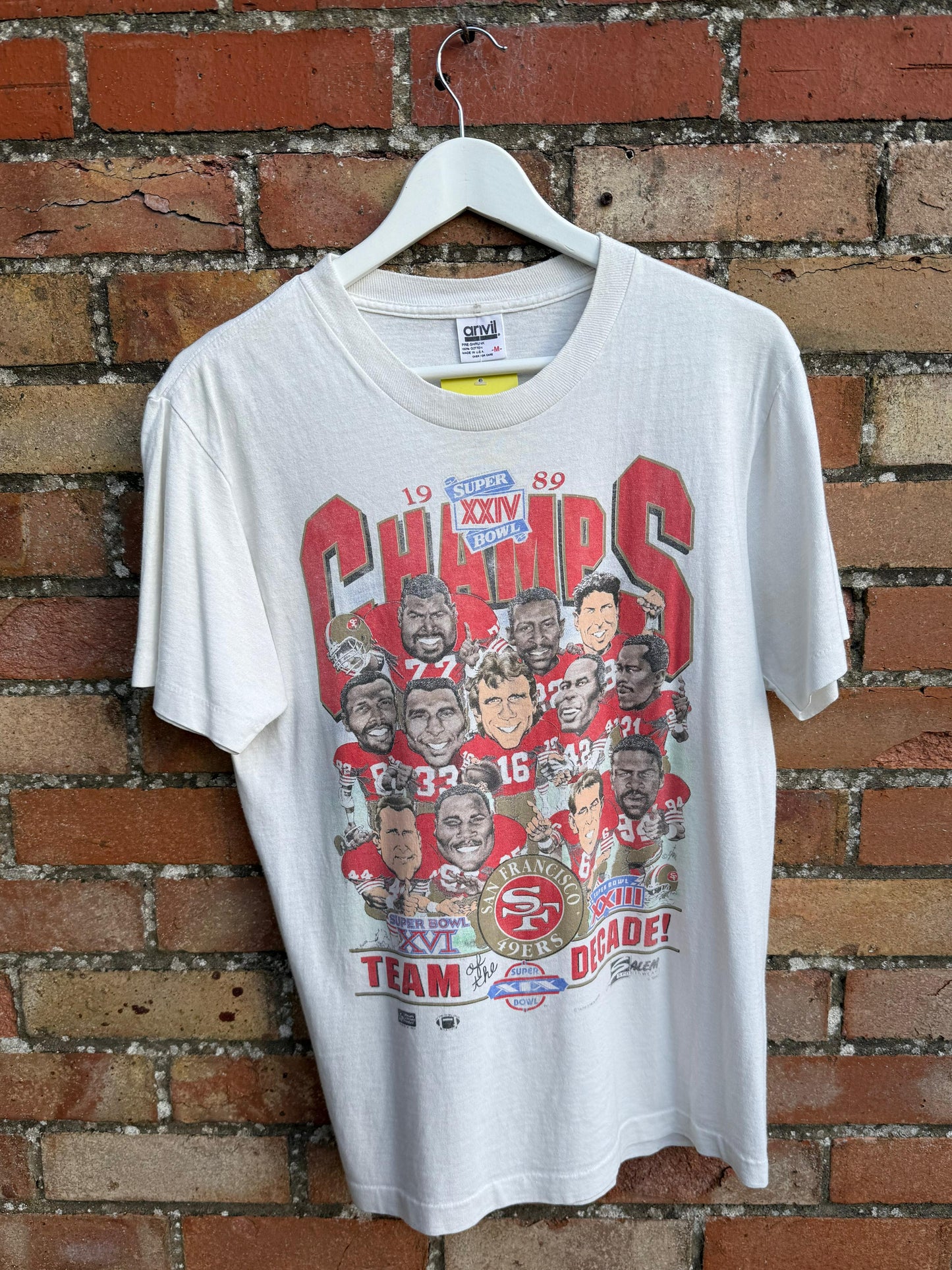 White t-shirt with San Francisco 49ers sports team graphic on a hanger against a brick wall