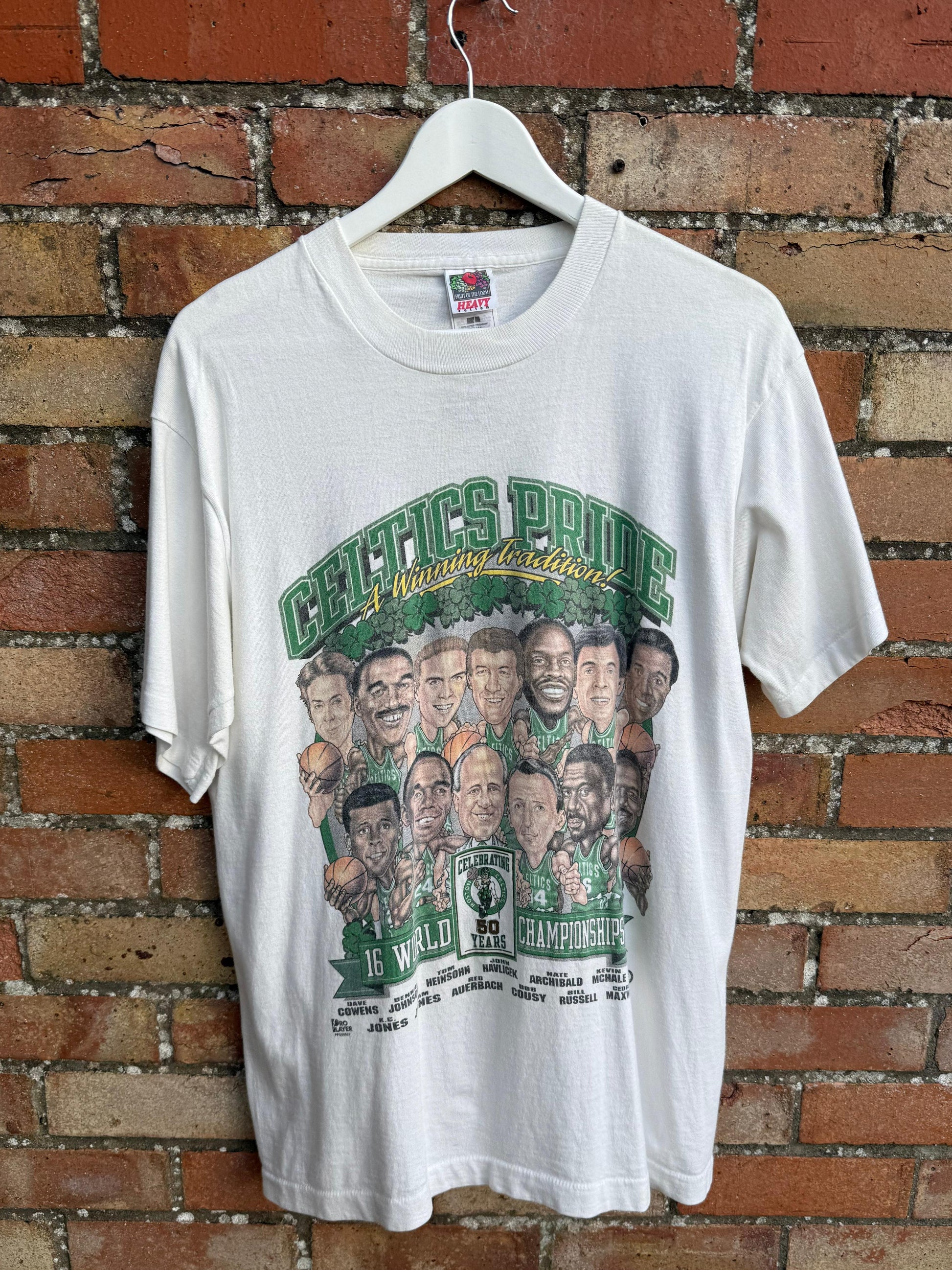 White t-shirt with Boston Celtics graphic design of World Championship Team, hanging on a brick wall.