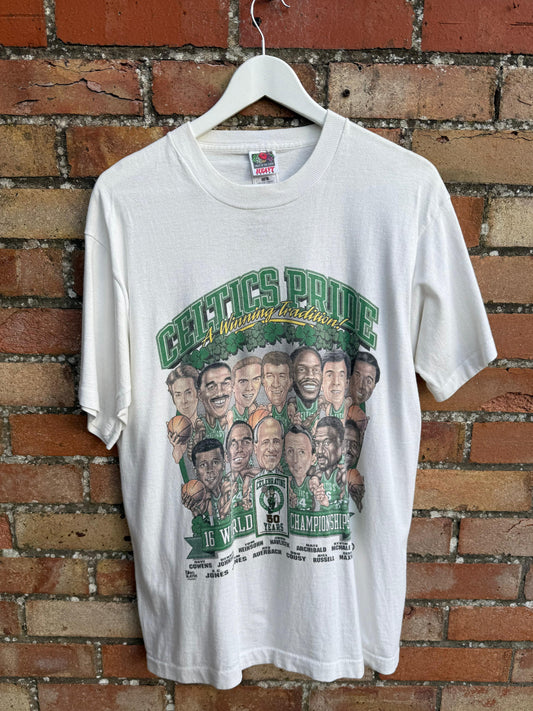 White t-shirt with Boston Celtics graphic design of World Championship Team, hanging on a brick wall.