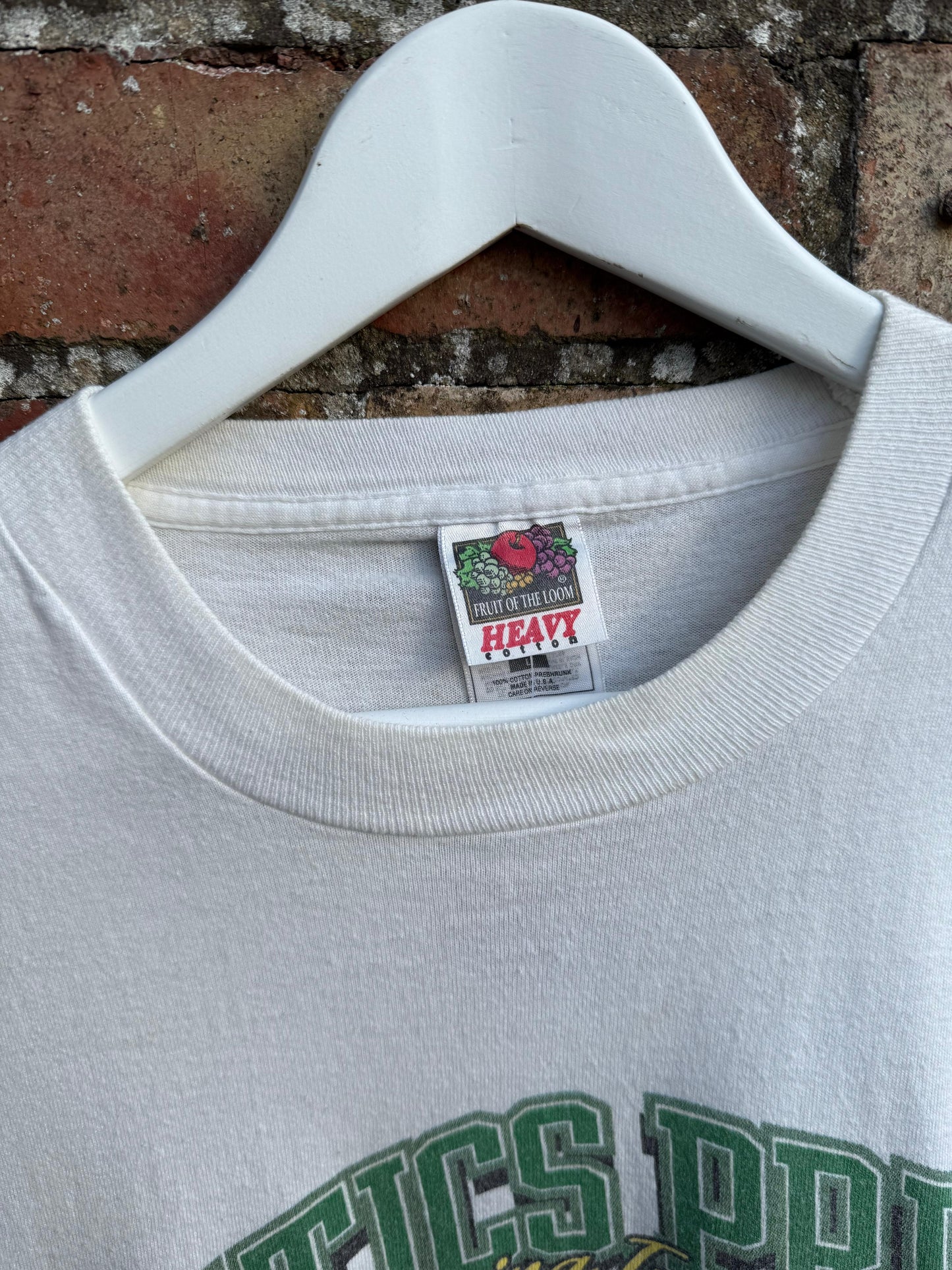 White sweatshirt with Fruit of the Loom  brand label and text Celtics Pride, on a hanger against a brick wall background