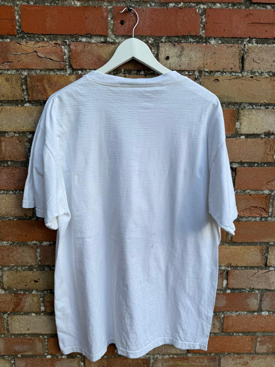 White t-shirt on a hanger against a brick wall
