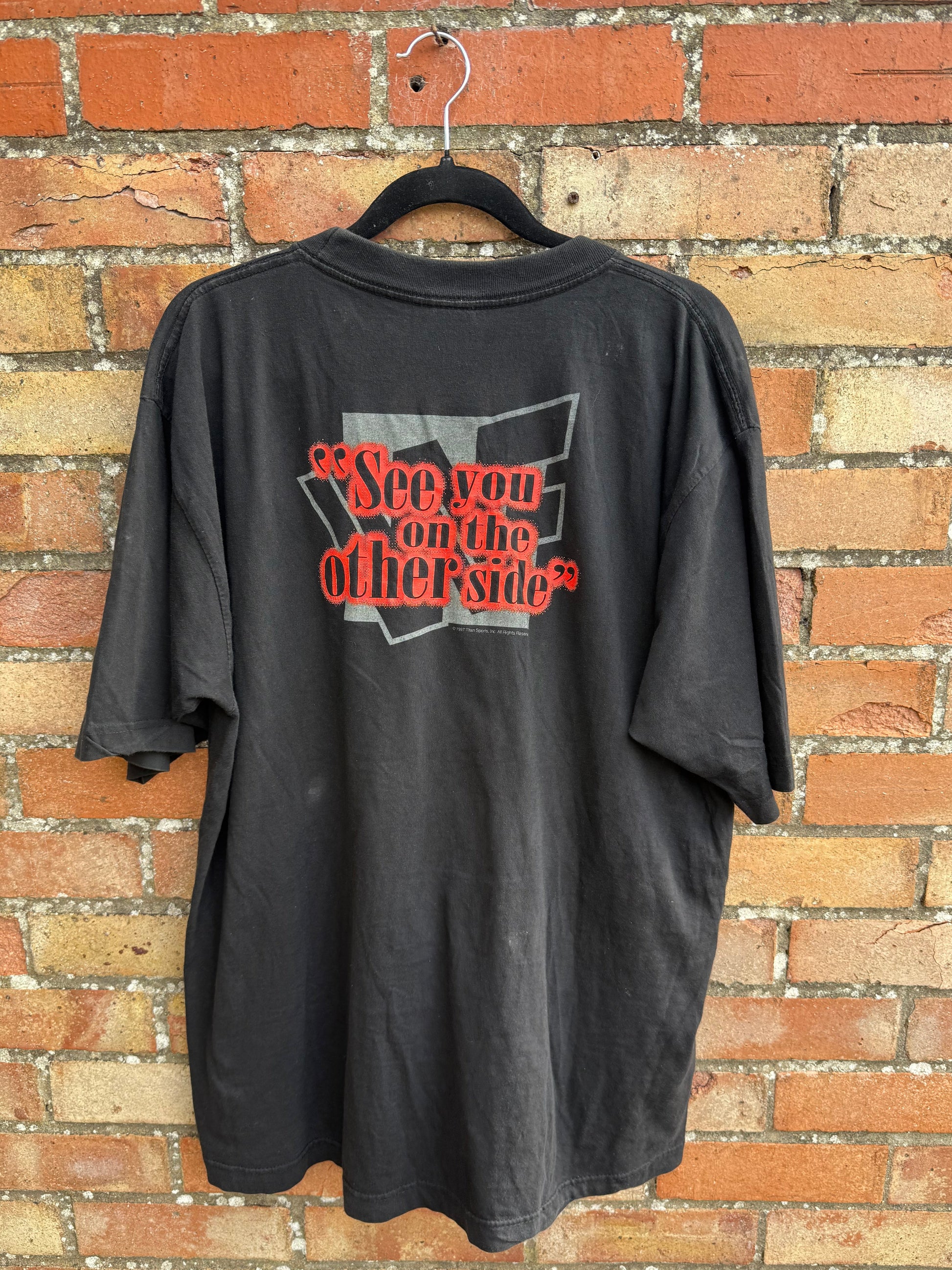 Bach of black t-shirt with red and white graphic 'See you on the other side', hanging against a brick surface