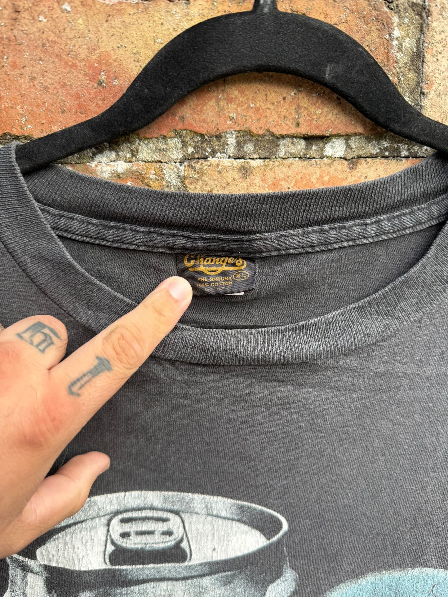 Black t-shirt with a Changes brand label on a hanger against a brick wall background