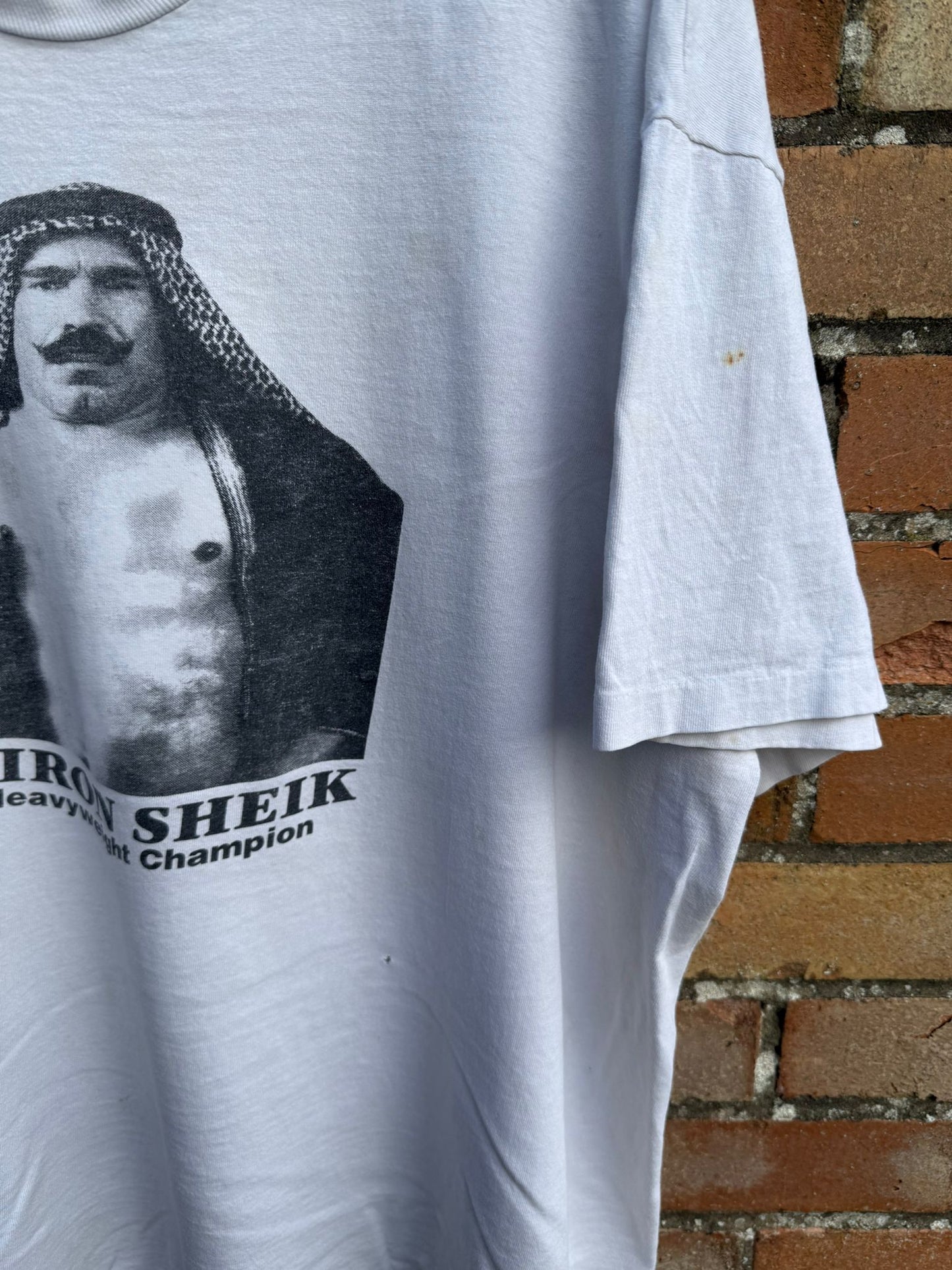 White t-shirt with Iron Sheik graphic against a brick wall