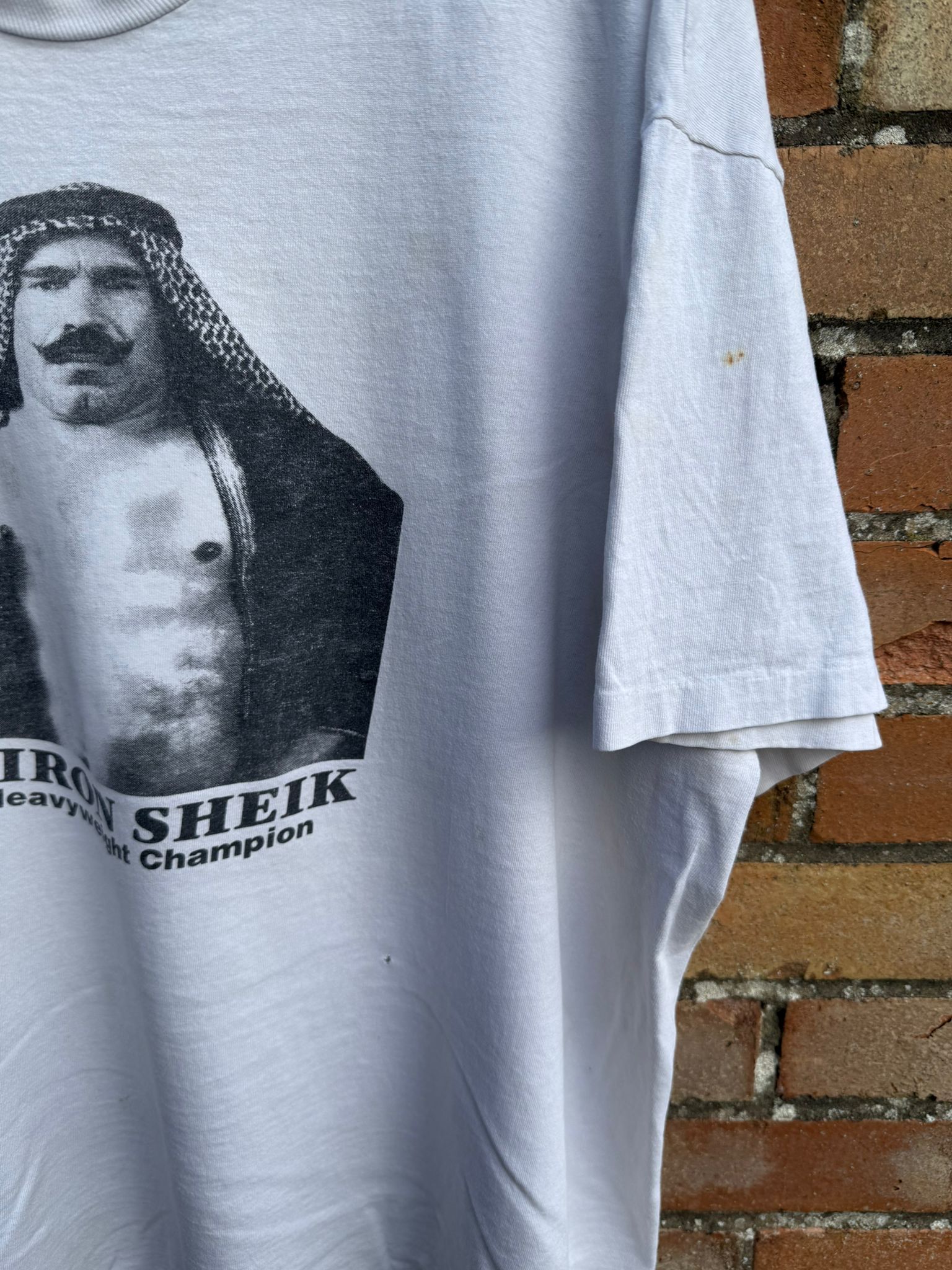 White t-shirt with Iron Sheik graphic against a brick wall
