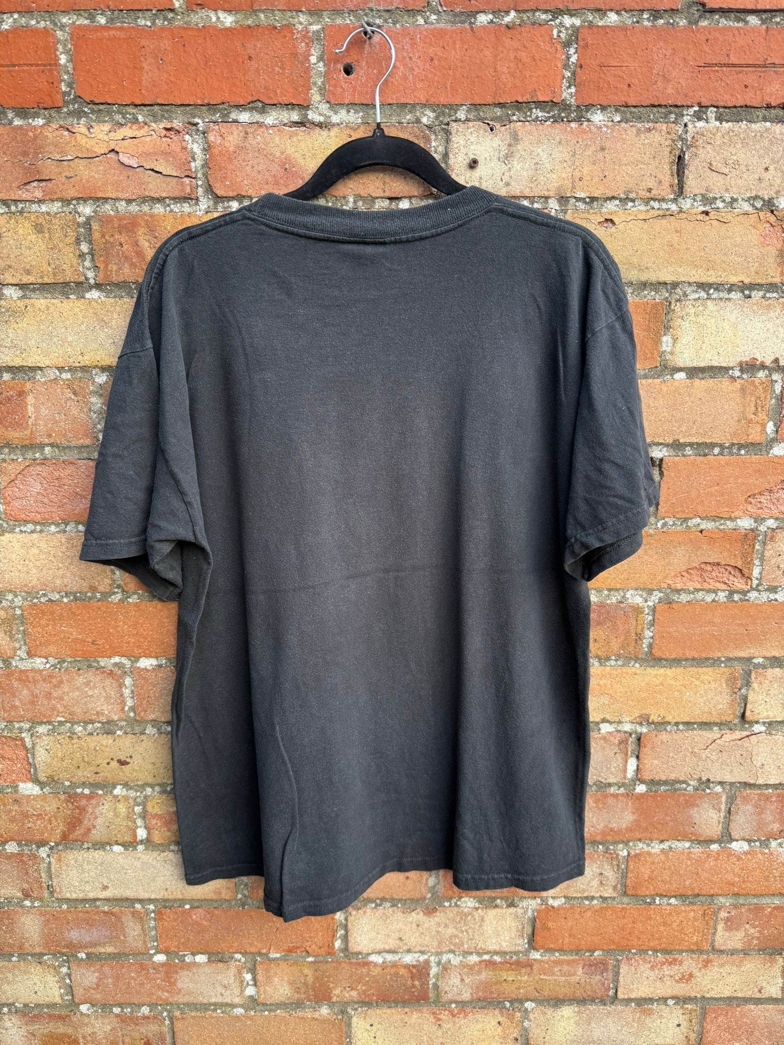 Black t-shirt on a hanger against a brick wall