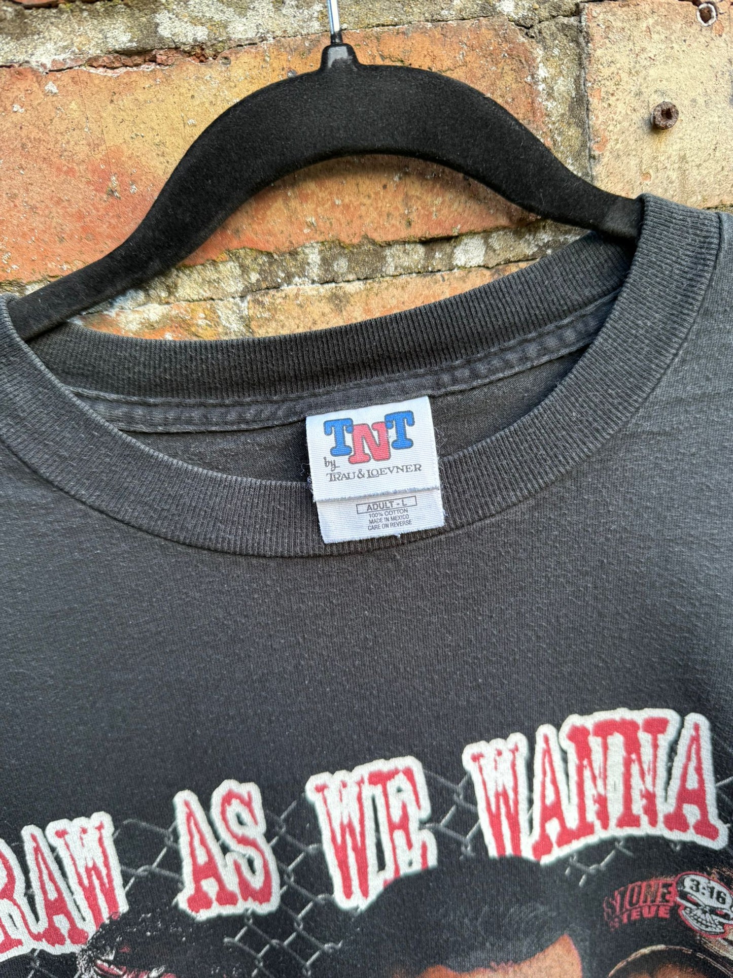 Black t-shirt with close up on a TNT tag by Trau & Loevner with red print on shirt Raw as we wanna be