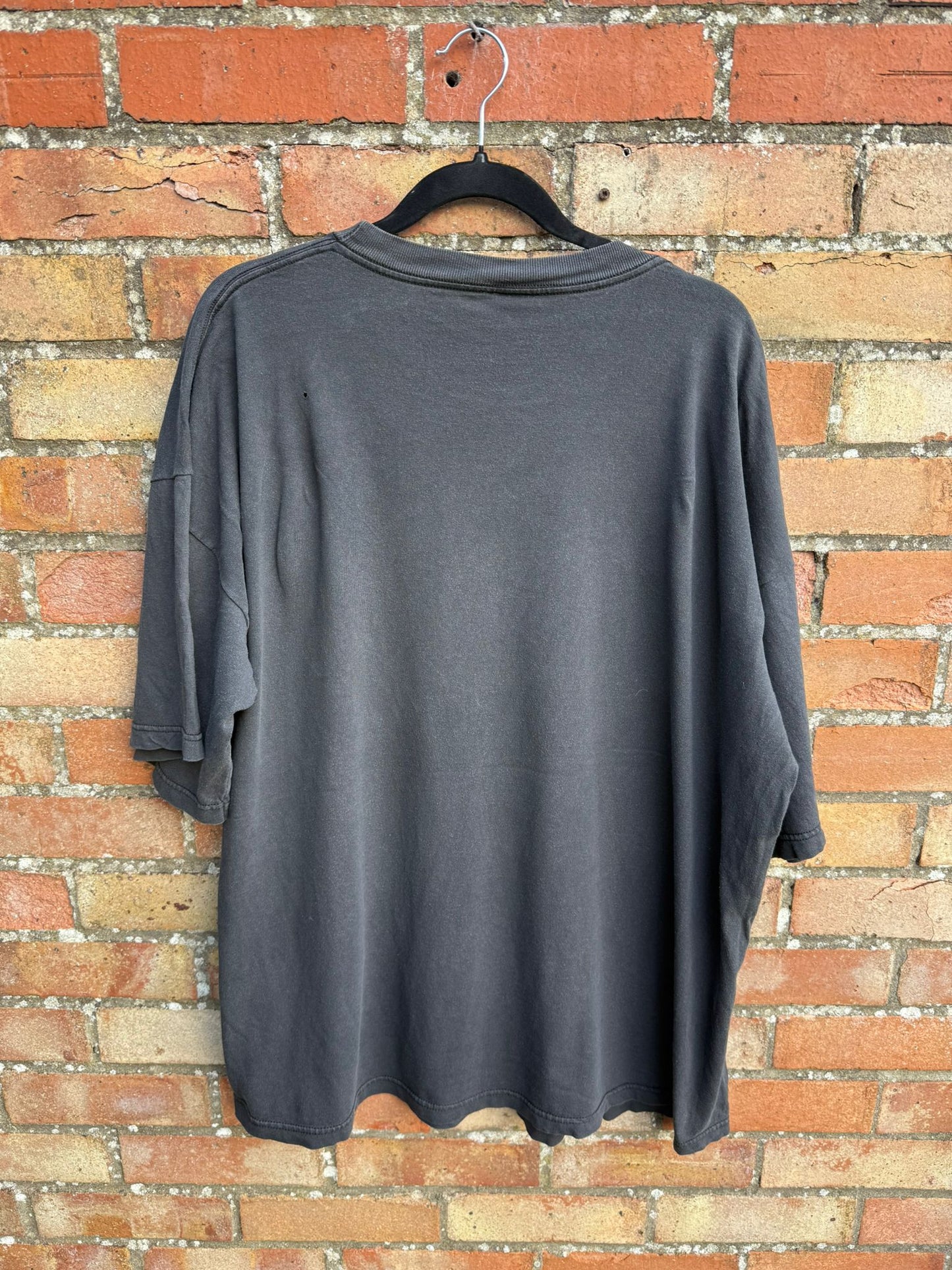 back image of a black -tshirt hanging against a brick wall