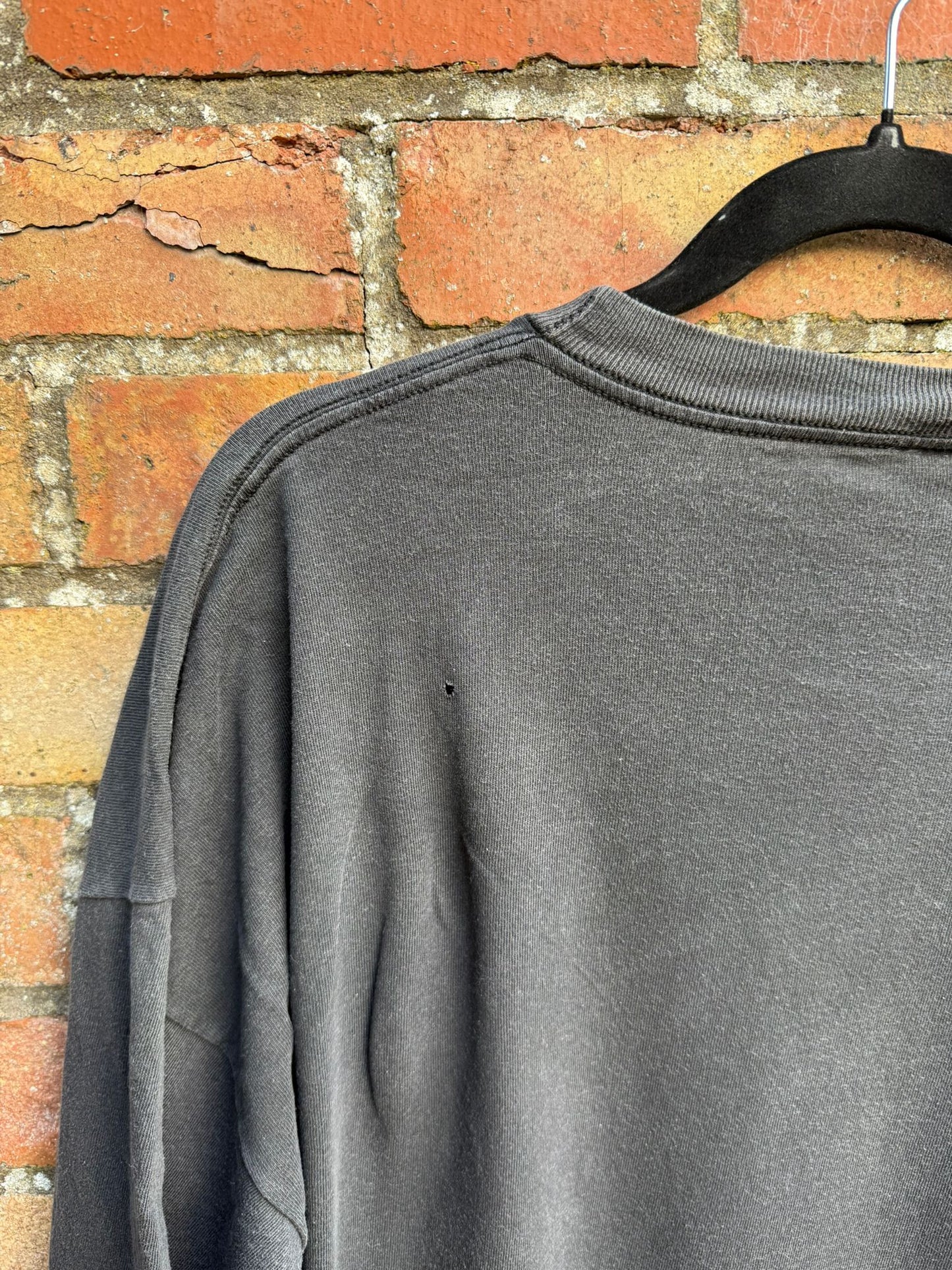 Back shoulder area of a black t-shirt showing a small pin hole