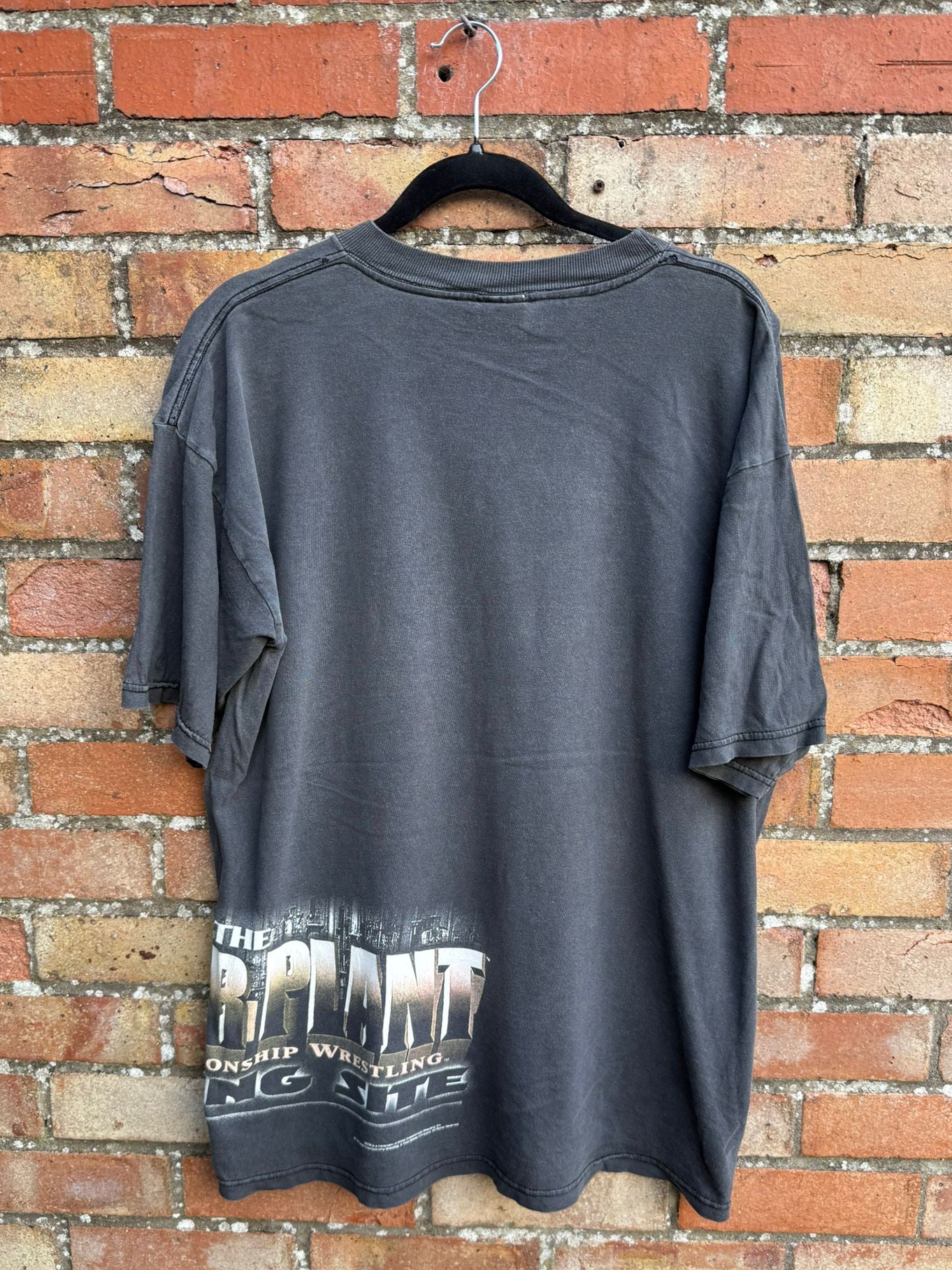 Black t-shirt hanging against a brick wall with branding on its bottom
