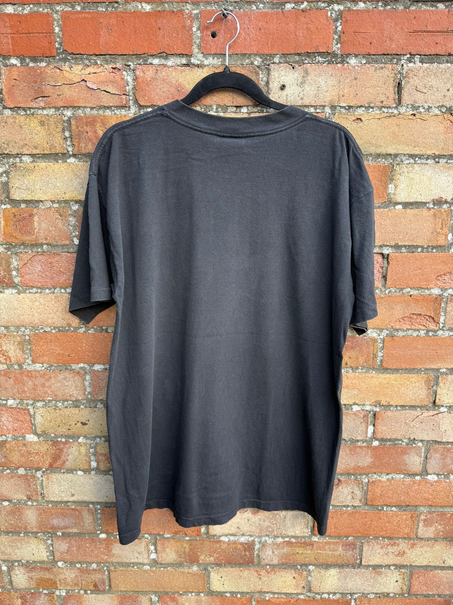 Back of a black t-shirt on a hanger against a brick wall