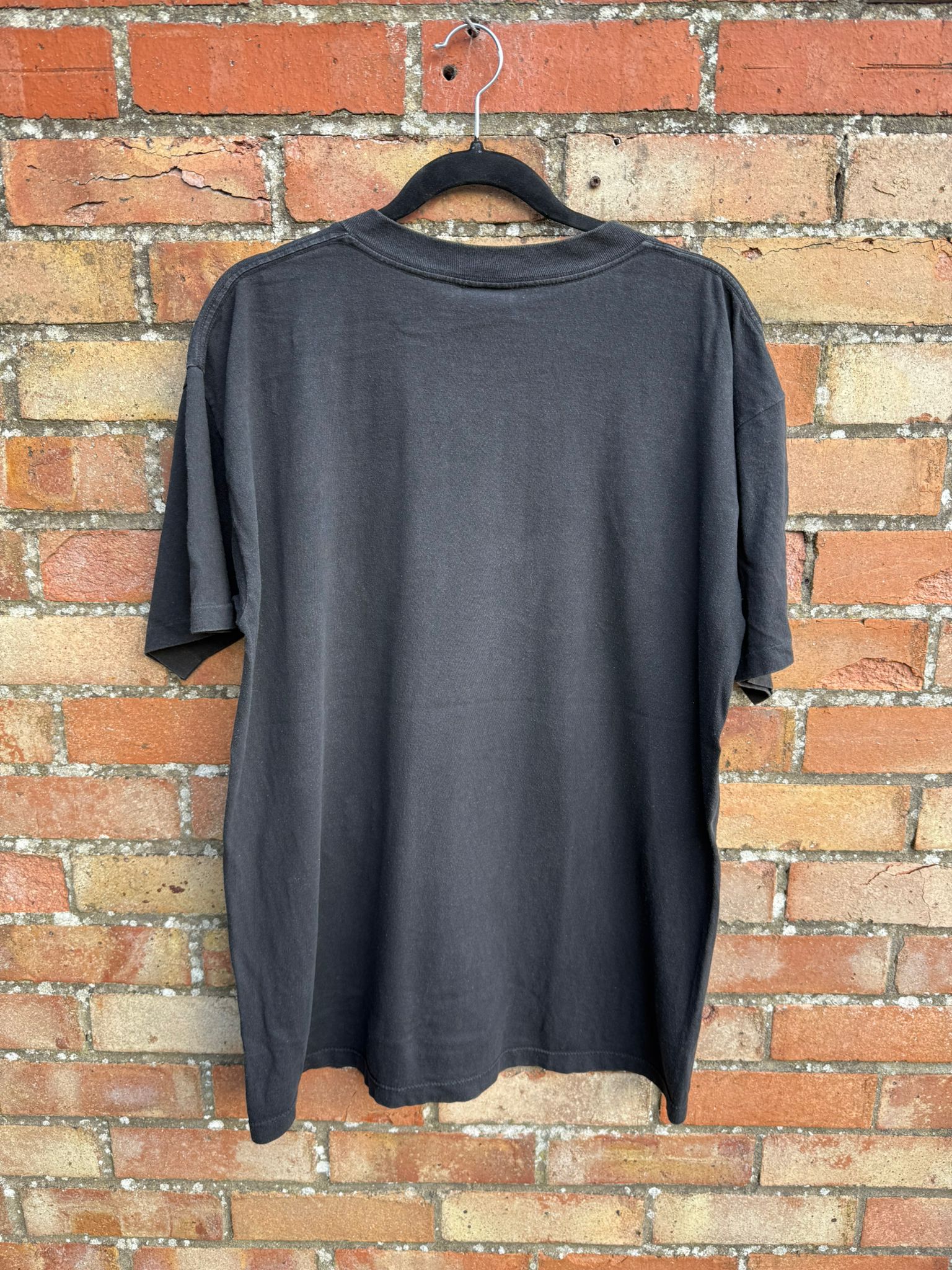 Back of a black t-shirt on a hanger against a brick wall