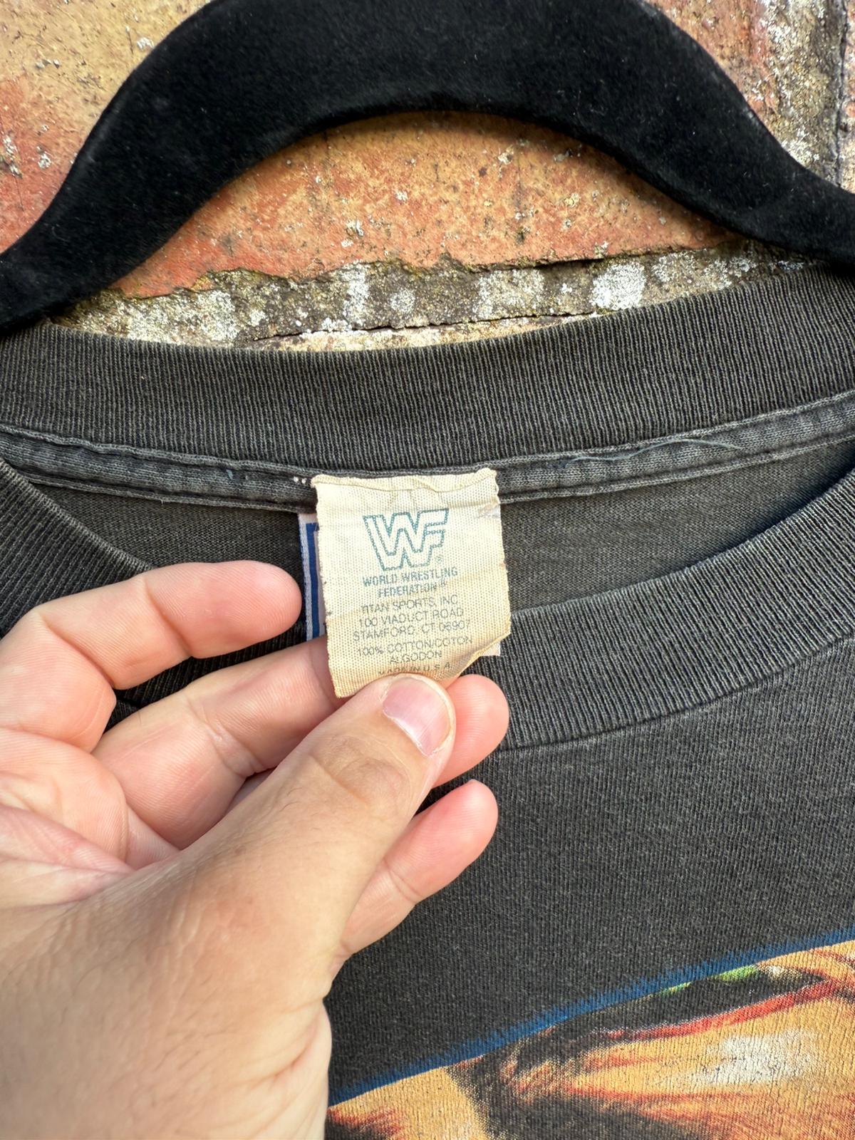 Close up of old WWF Titan Sports tag on a black t-shirt, against a brick wall background.