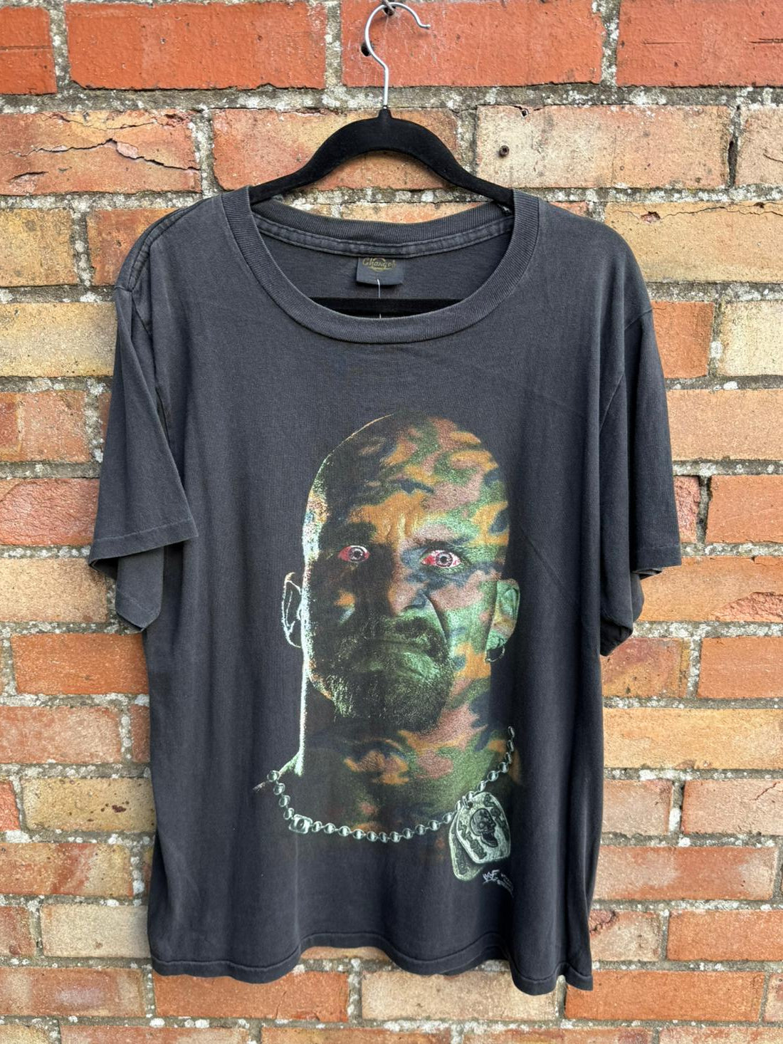 Black t-shirt with graphic design of a camouflaged face on a brick wall background
