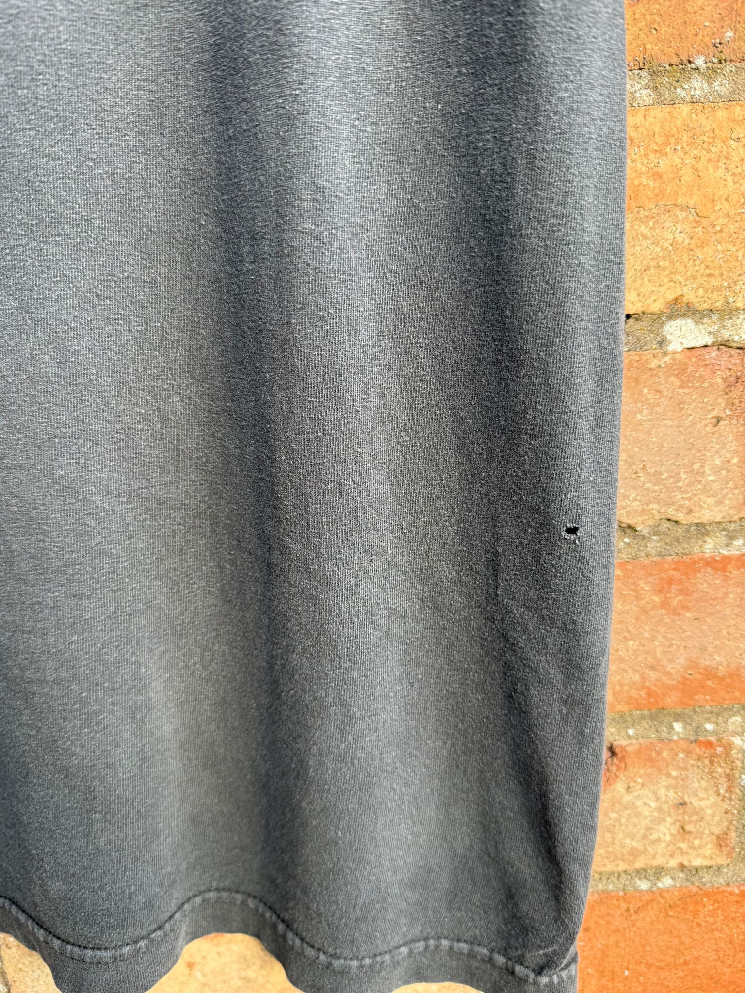 Black t-shirt with close-up of bottom area with a small pinhole showing