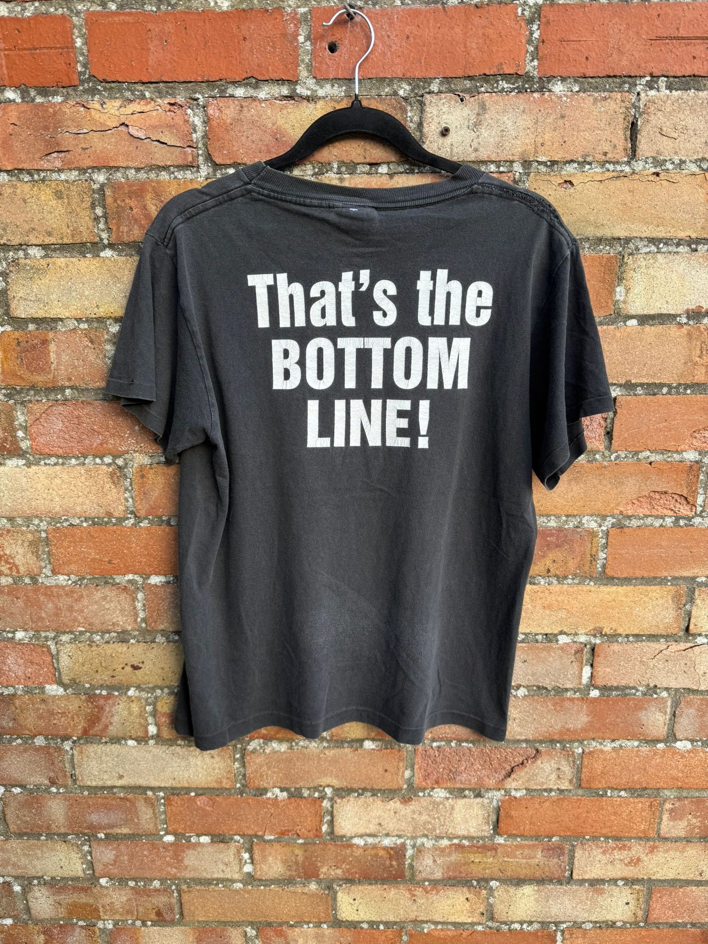 Black t-shirt with 'That's the BOTTOM LINE!' text on a brick wall background