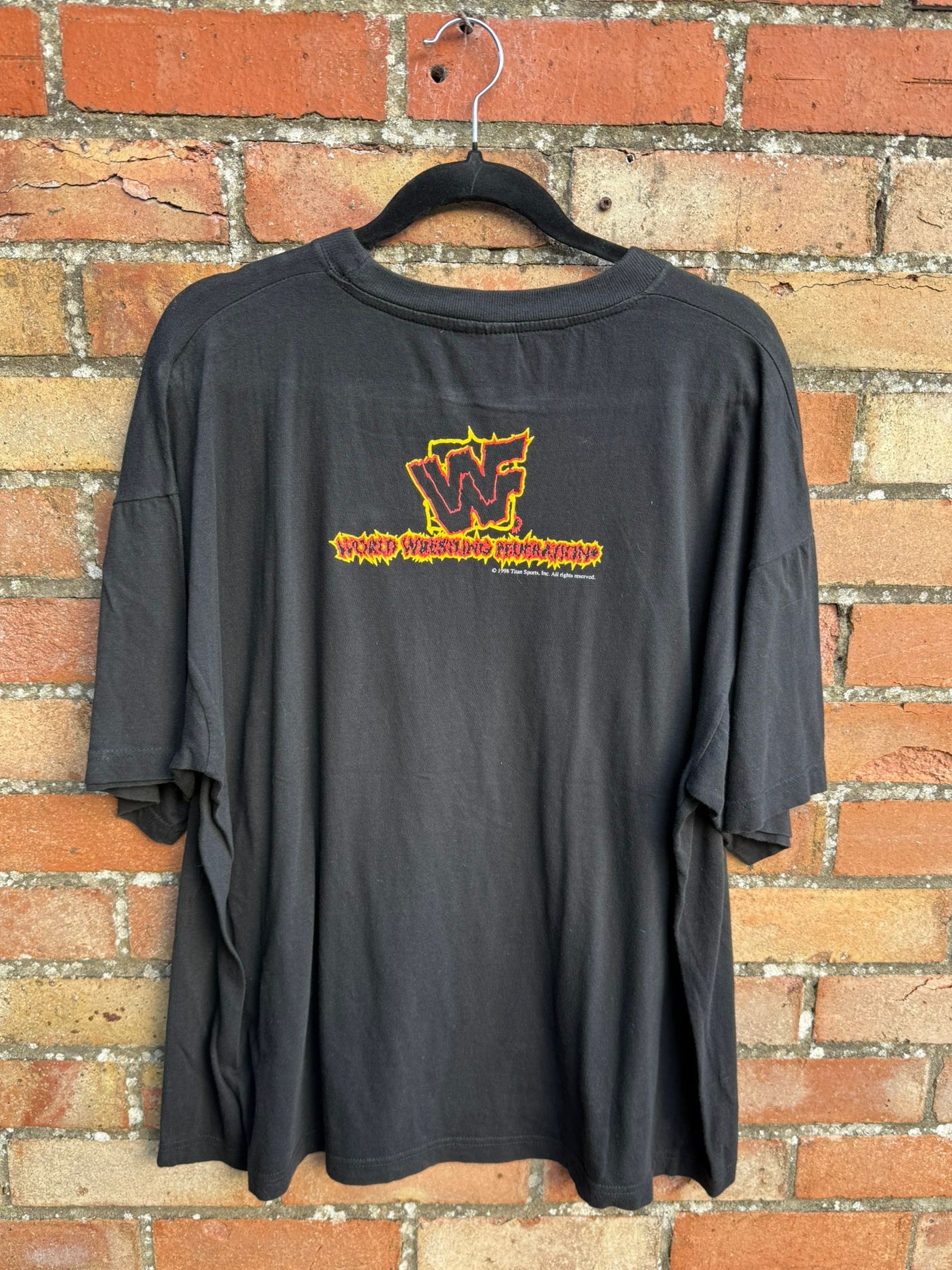 Black t-shirt with a WWF in flames logo on a hanger against a brick wall