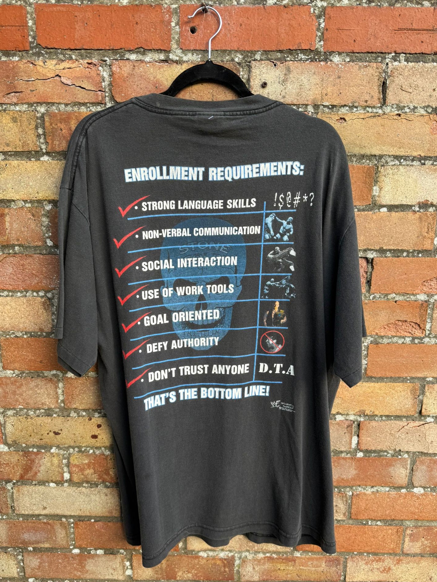 Black t-shirt with Enrollment Requirements text and graphics on a brick wall background