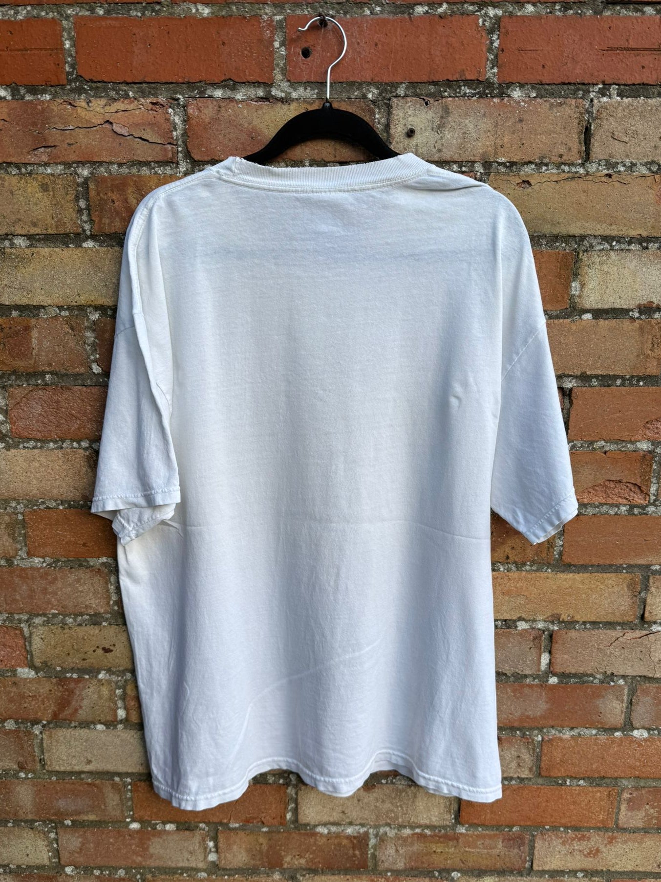Back view of a white t-shirt on a hanger against a brick wall
