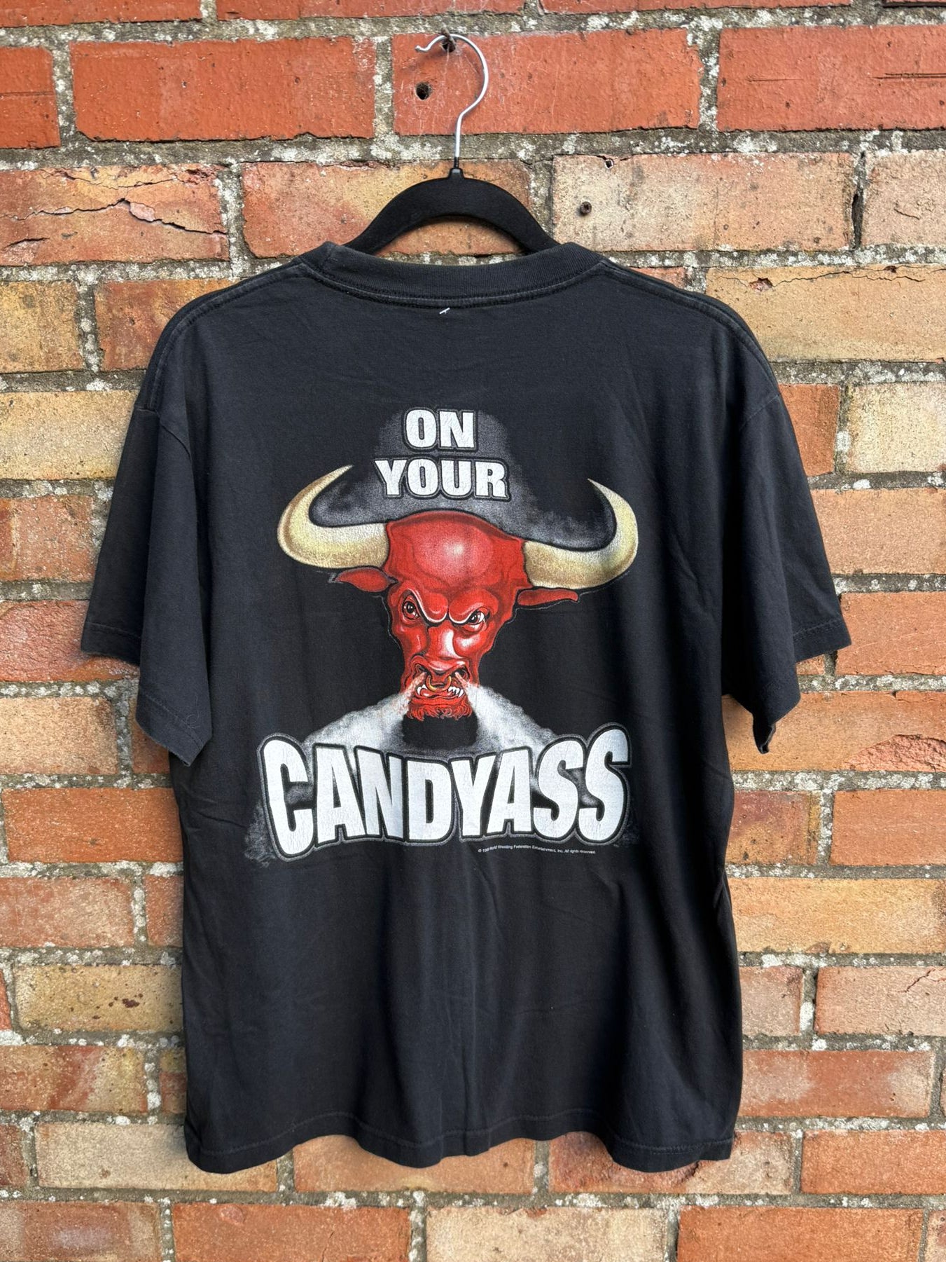 Black t-shirt with graphic bull design and On Your Candyass text hanging on a brick wall background
