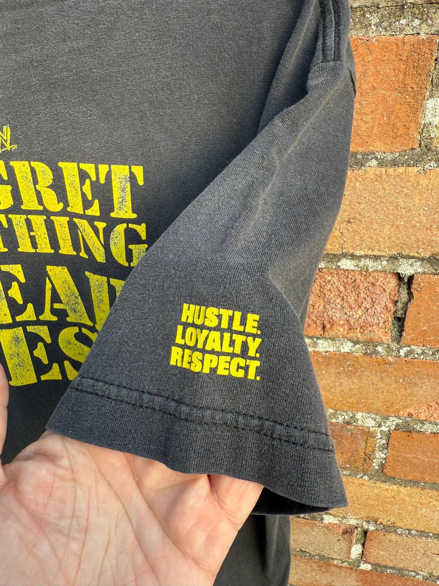 Black wrestling t-shirt sleeve hit with yellow text 'HUSTLE LOYALTY RESPECT' 