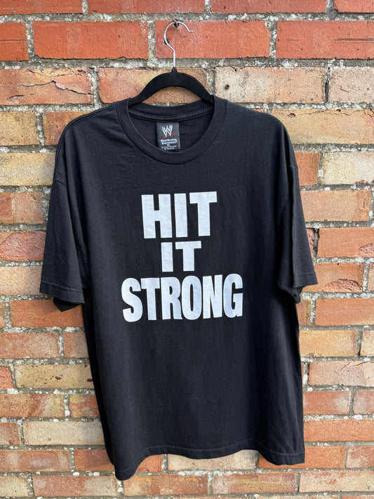 Black t-shirt with white large print Hit it Strong hanging against a brick wall