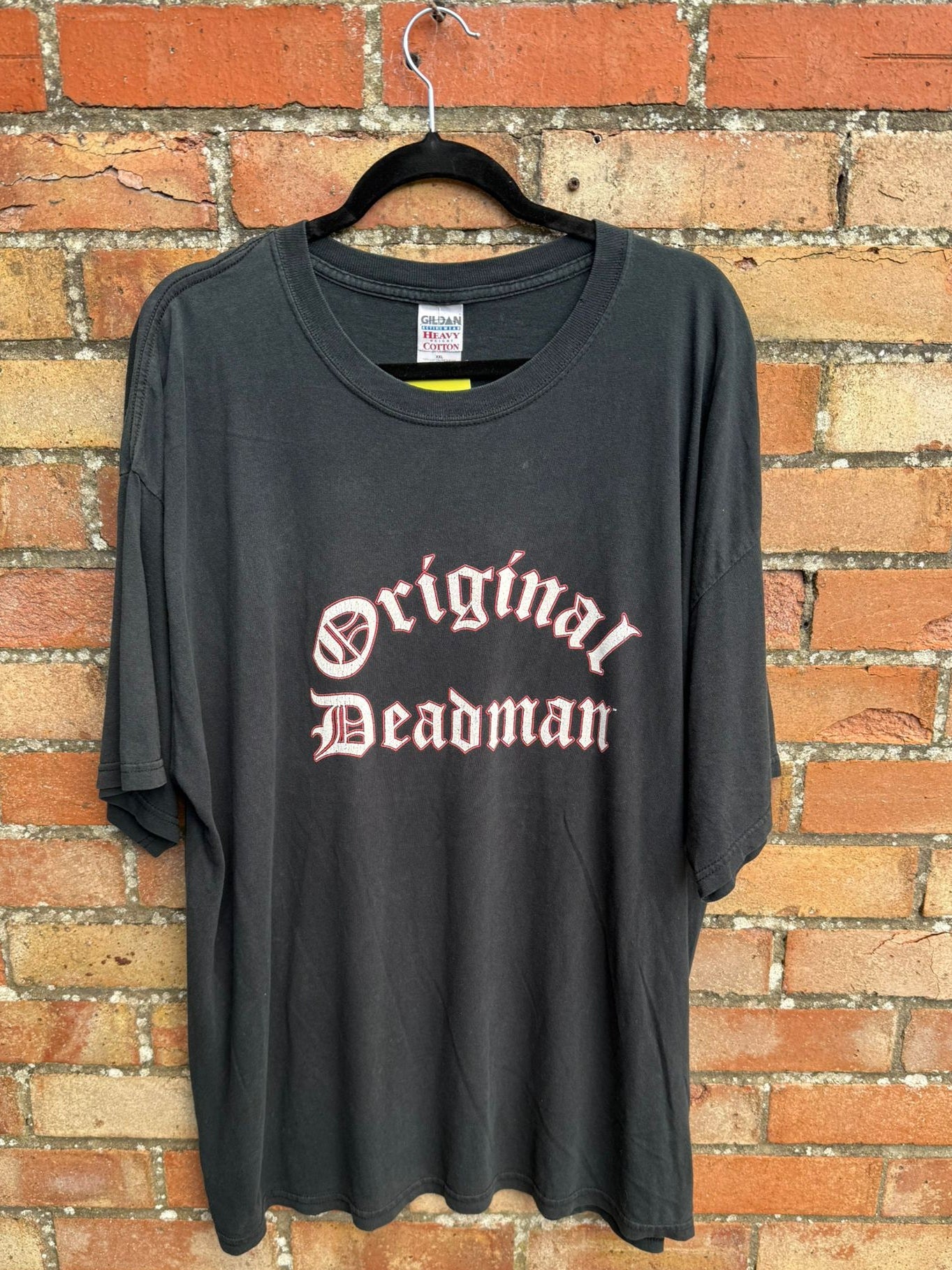 Black t-shirt with 'Original Deadman' text and Gildan tag on a brick wall background