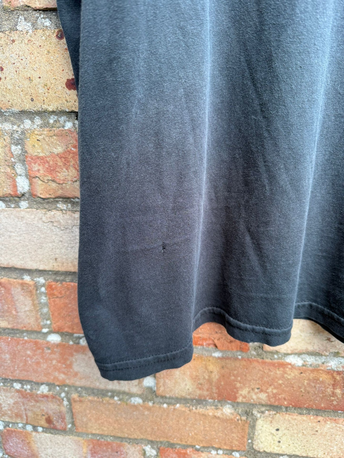 Close-up of bottom portion of black t-shirt showing a pinhole in material