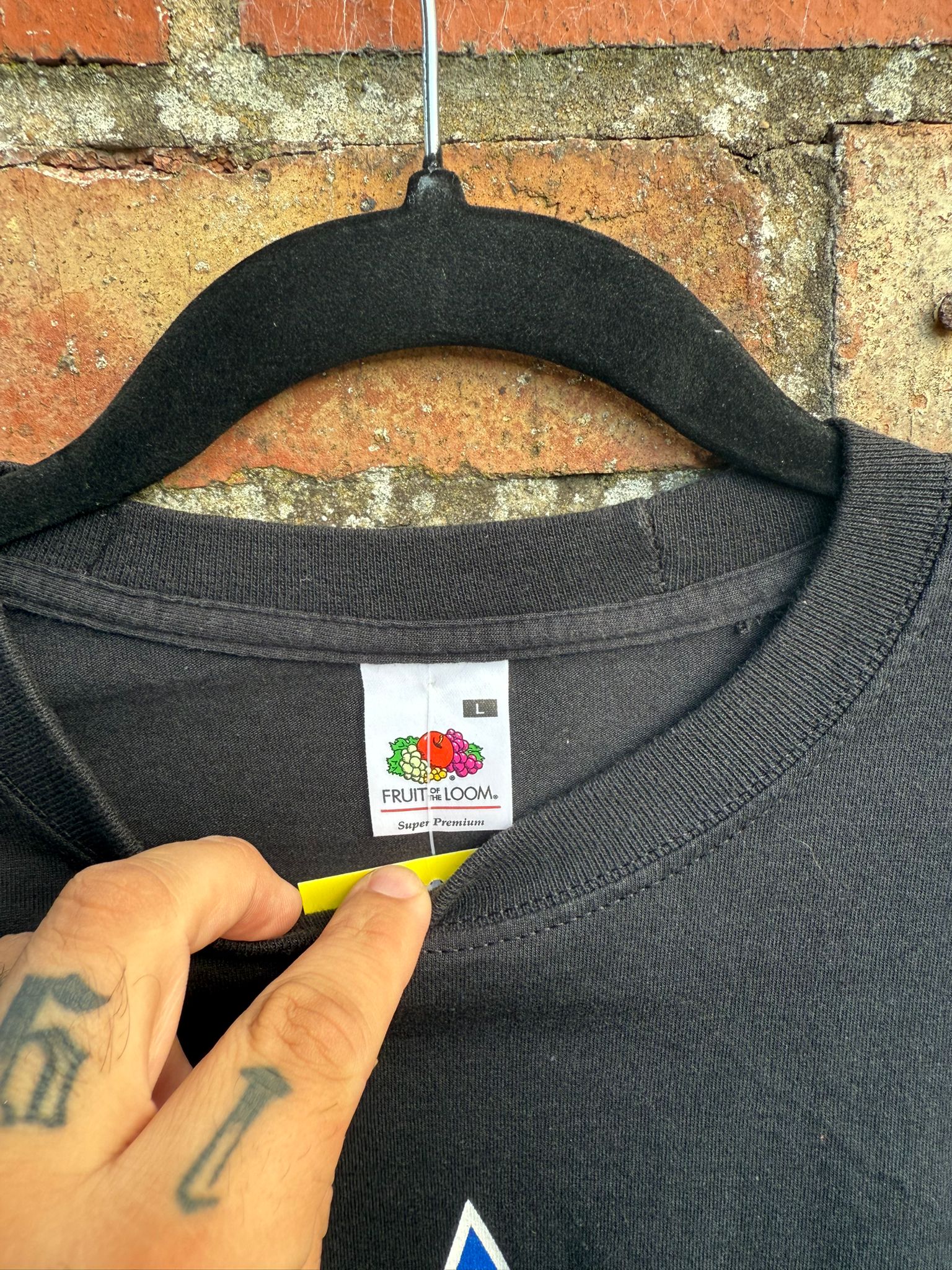 Close-up of Fruit of the Loom clothes tag on a black t-shirt hanging against a brick wall