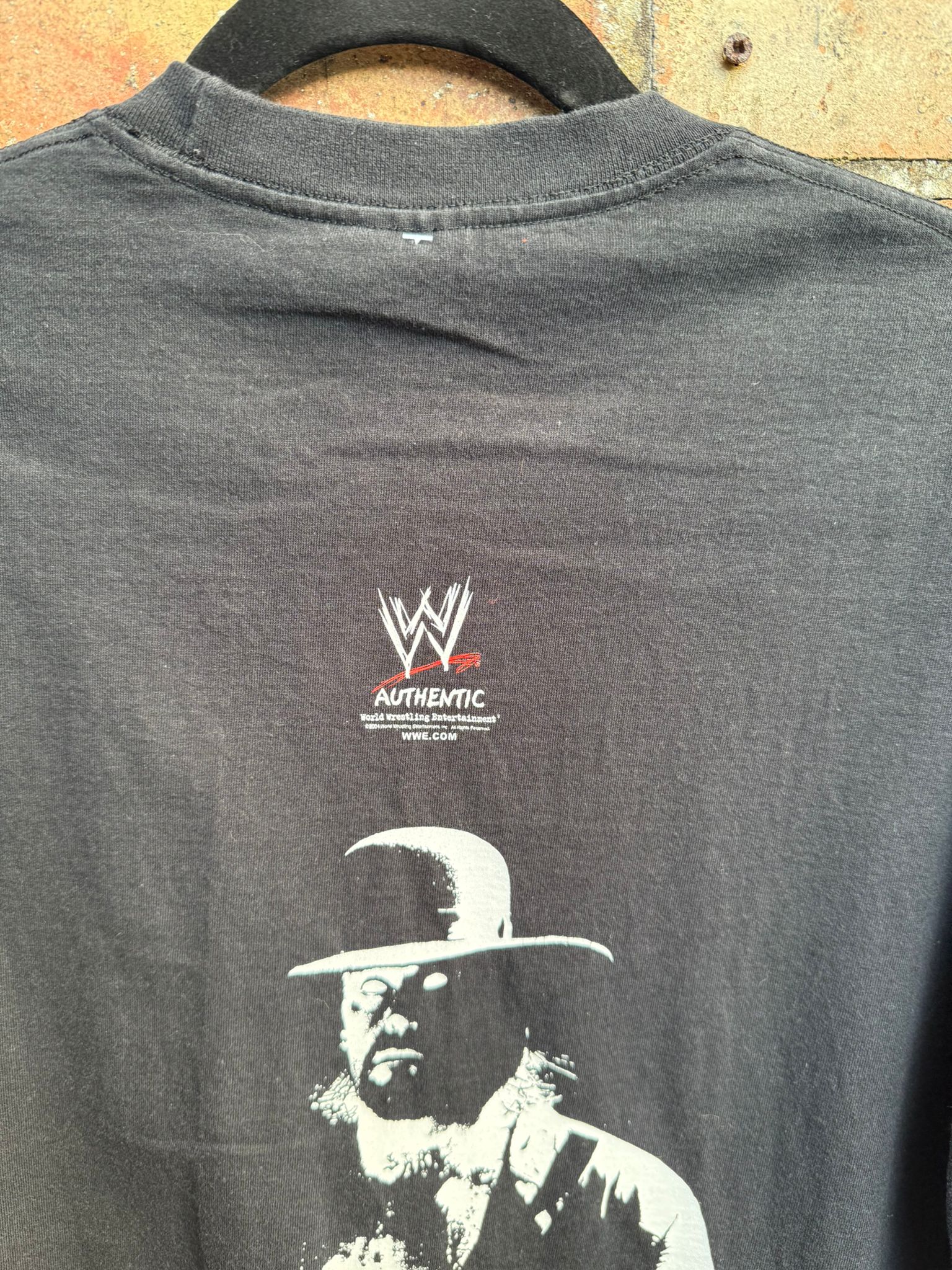 Black t-shirt with WWE Authentic logo and graphic of the Undertaker wearing a hat.
