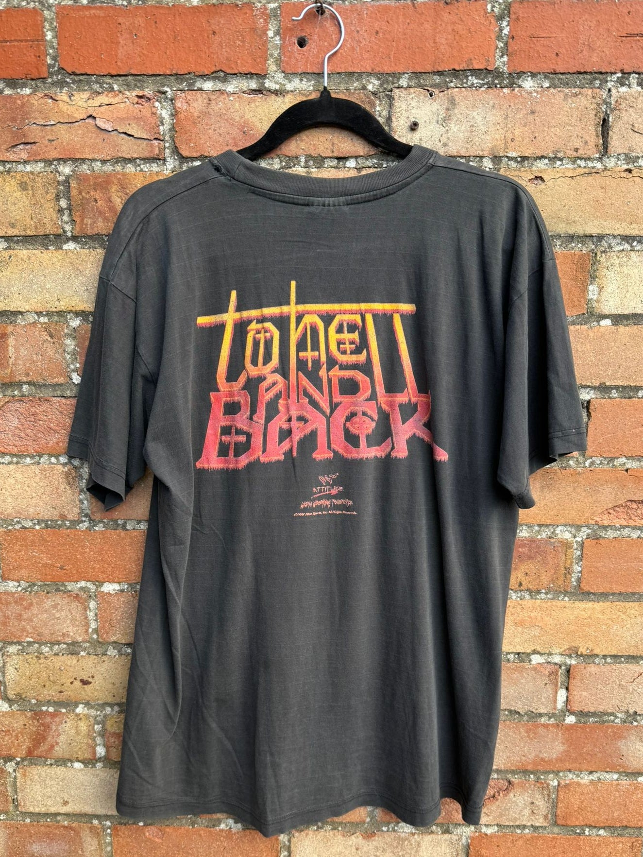 Back view of a black t-shirt with to hell and back red and yellow text on a brick wall background